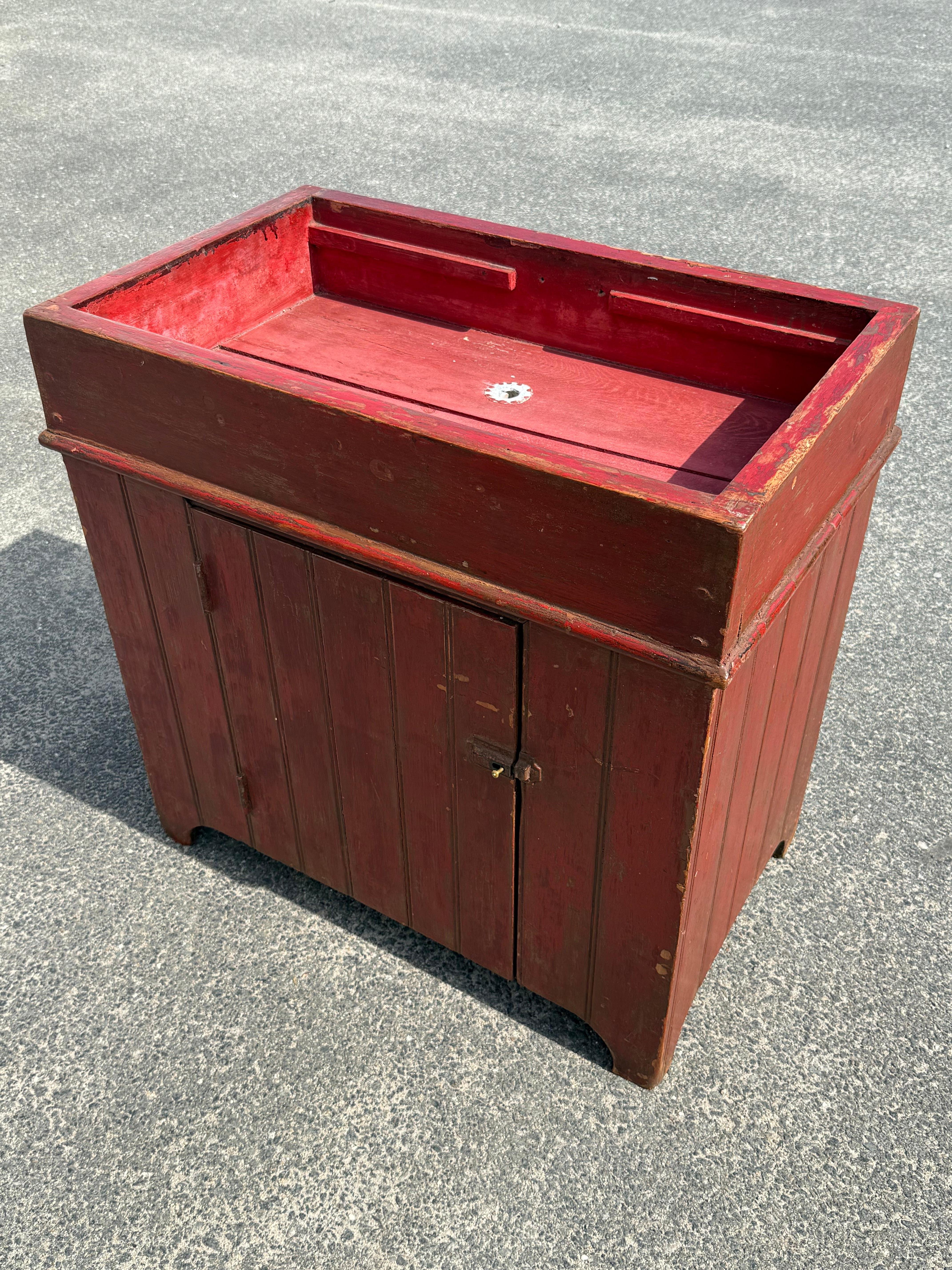 Diminutive 19th century pine dry sink in original red paint.  Sink section with old drain, case with vertical paneling.  Single drawer on front reveals interior compartment with shelf at left.  