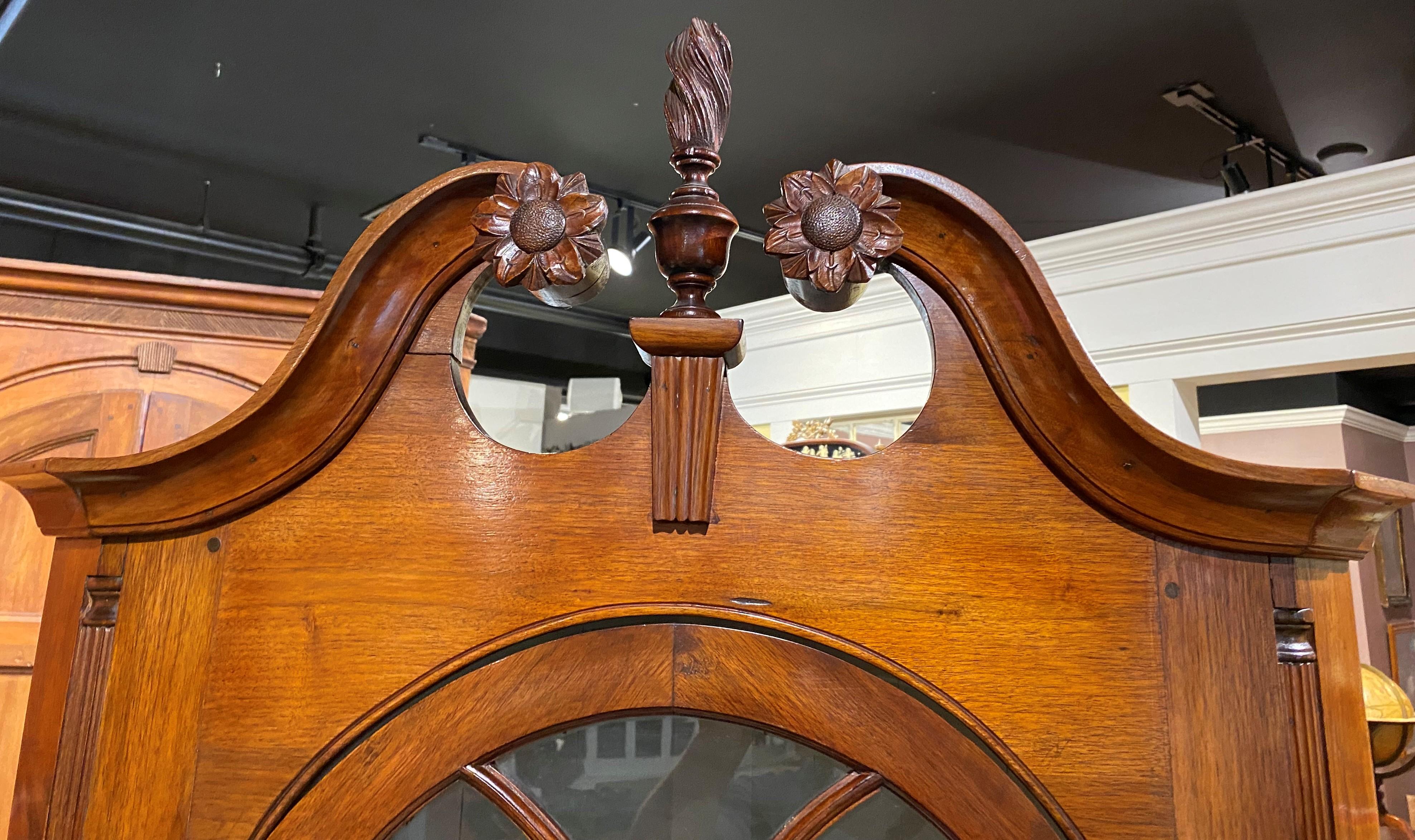 A petite two-part cherry corner cupboard, its upper case with a split arched pediment with carved rosettes and central urn spiral flame finial surmounting an arched glass door with glazed panels, opening to a gray painted two shaped shelf interior,