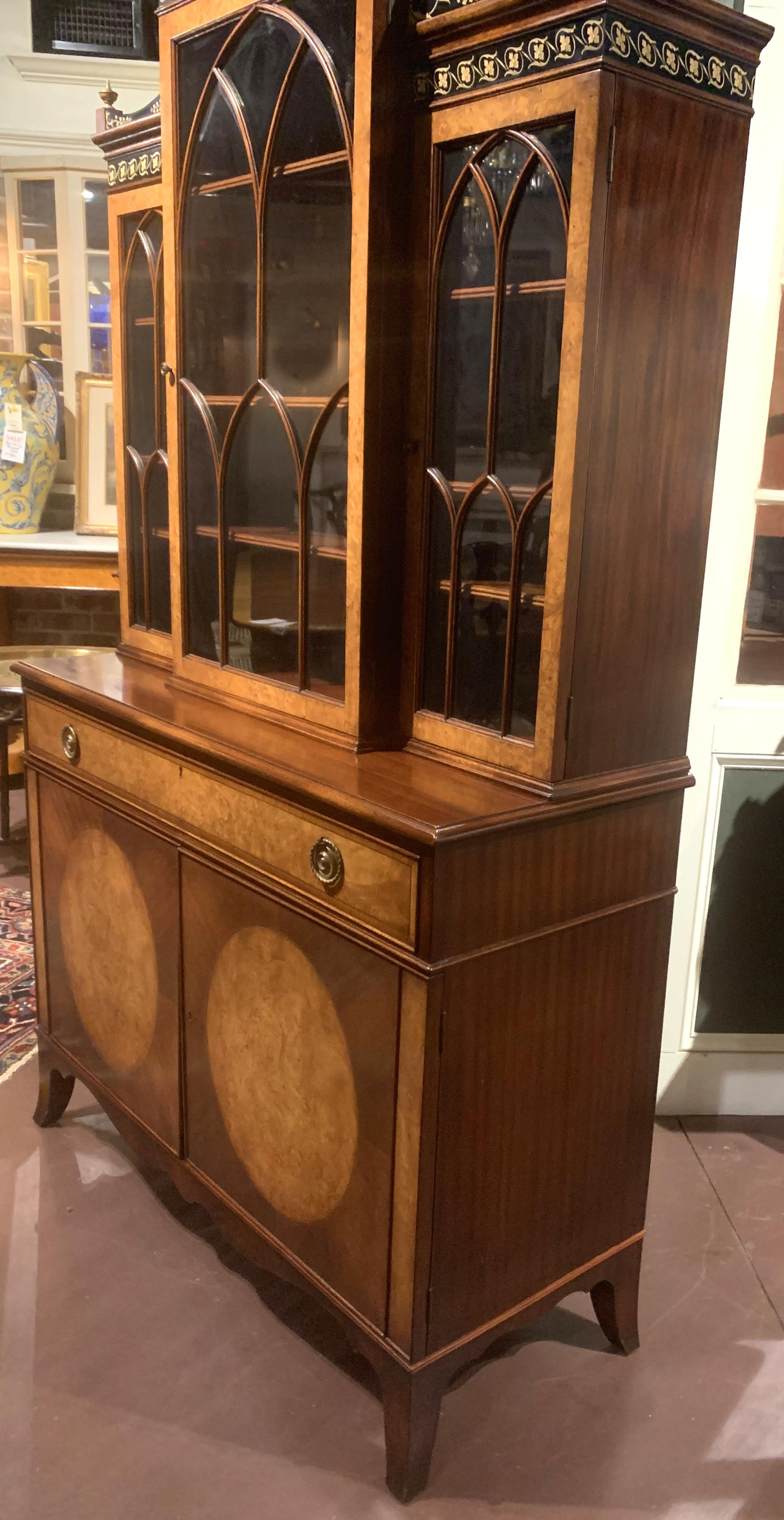 A fine diminutive two section Adam style bookcase or china cabinet, its upper section featuring a foliate carved gilt crest, four urn form finials, and hand painted Classical frieze surmounting three satinwood or light burled wood banded glazed