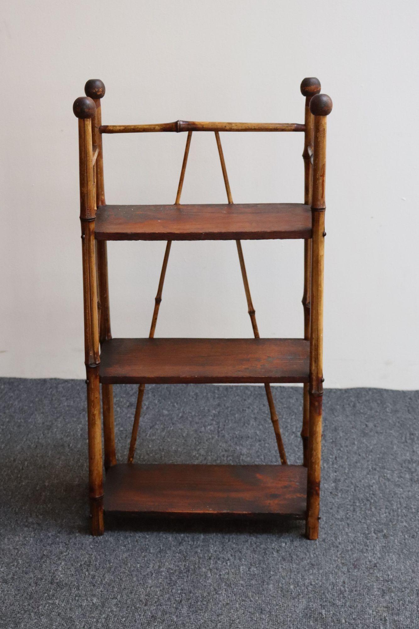 Petite étagère antique à trois niveaux (vers le début du 20e siècle, États-Unis).
Composé d'un cadre en bambou avec des ferrures en métal supportant trois étagères en noyer et orné de fleurons ronds sculptés à la main.
Etagère étroite et basse