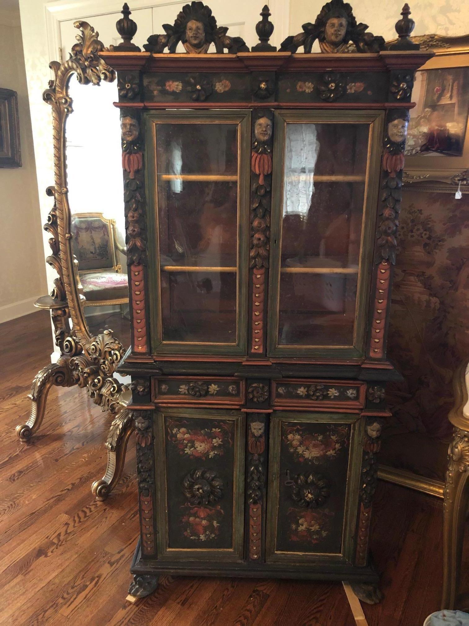 Italian, 19th century, two-part form, all-over dark green and olive original painted field, with floral highlight and applied polychrome painted putti, the upper case featuring a crest with two putti heads divided by three finials, above two