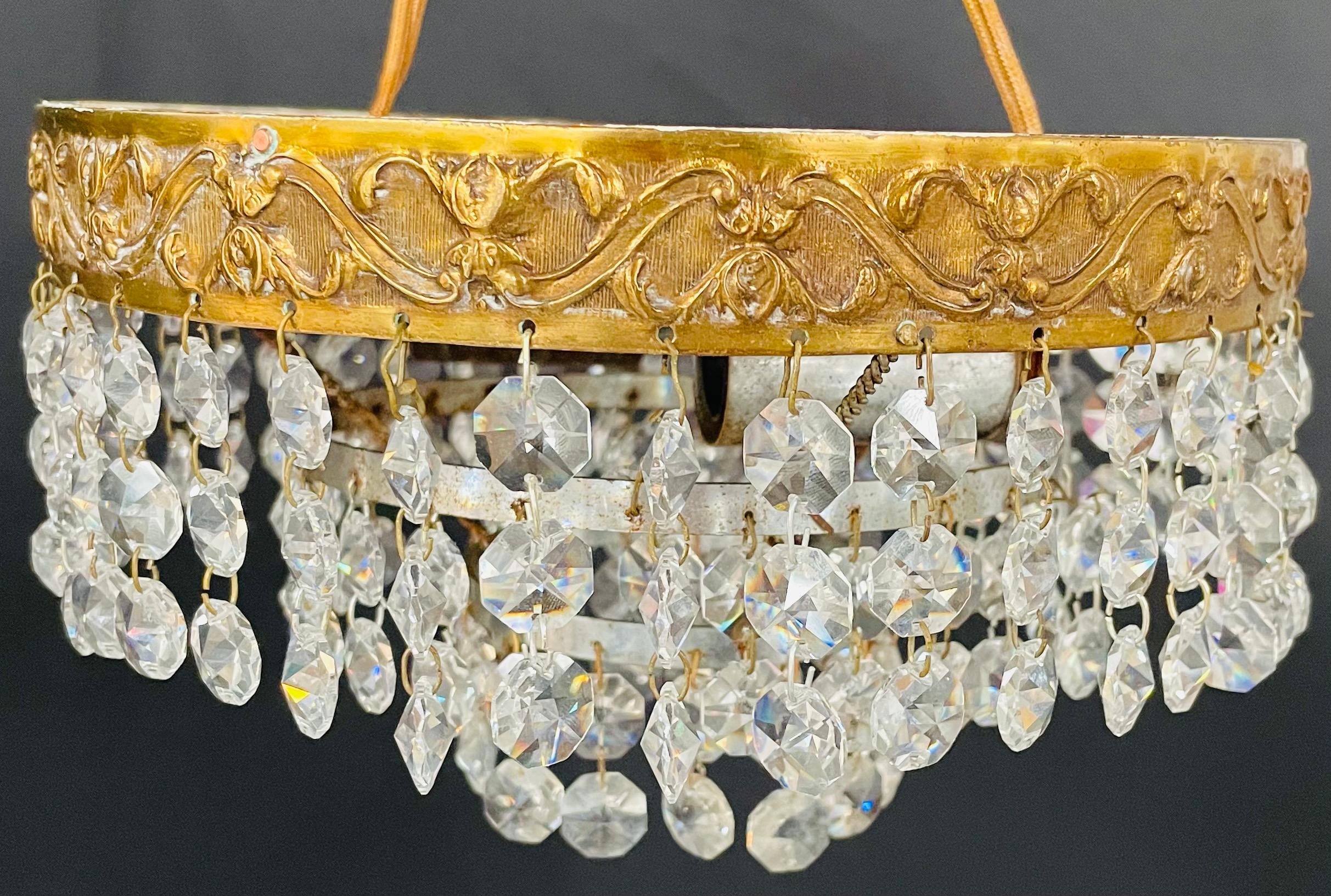 A French Regency style diminutive crystal chandelier. The circular shaped small chandelier features a brass band finely decorated and crystal prisms hanging from the band and from inside the chandelier. Perfect for hallway, small space or a bathroom