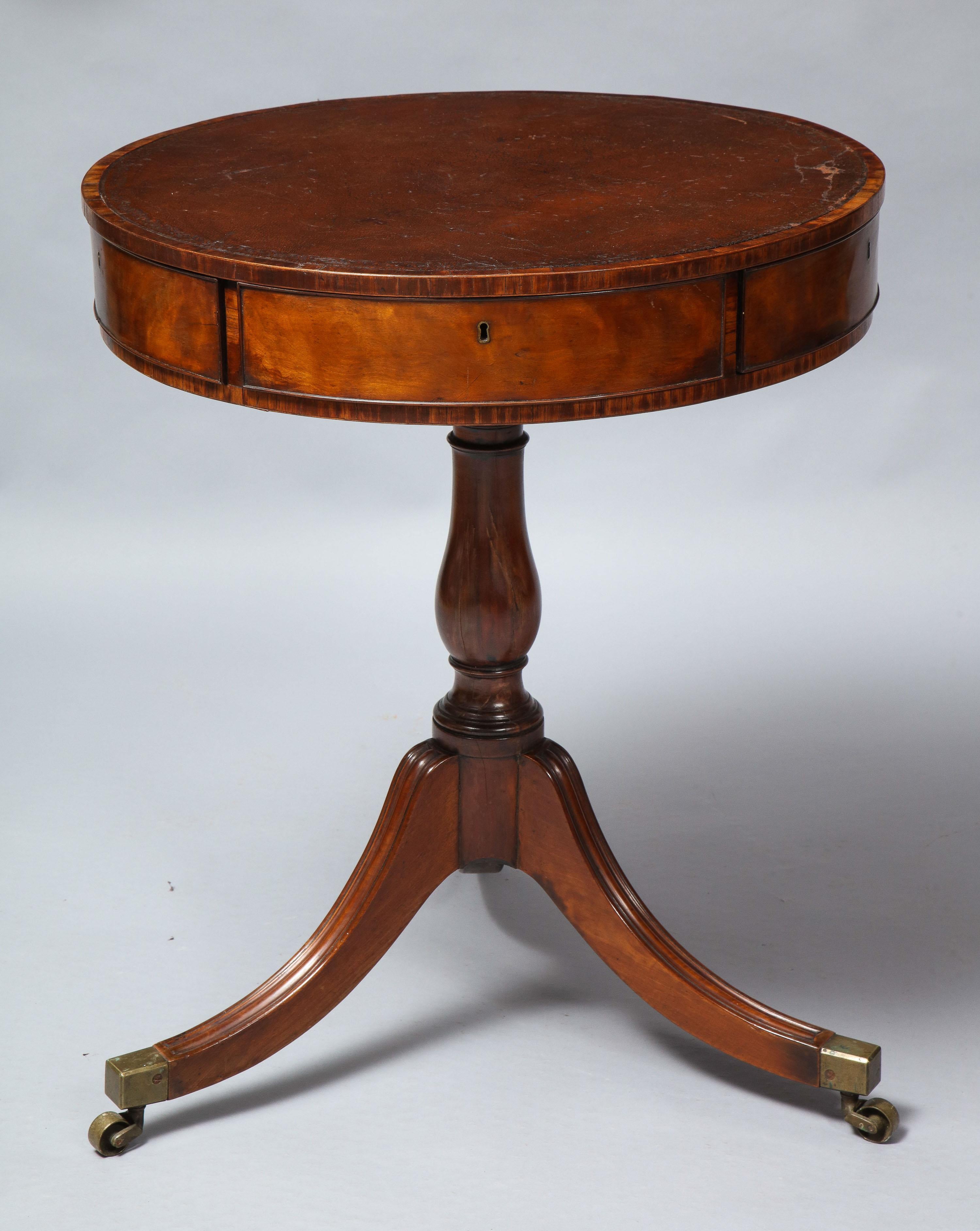 Fine George III period drum table, the distressed tooled leather top with rosewood cross banding, the four wedge shaped drawers with vividly grained mahogany fronts and retaining original locks and escutcheons, supported by turned mahogany shaft and