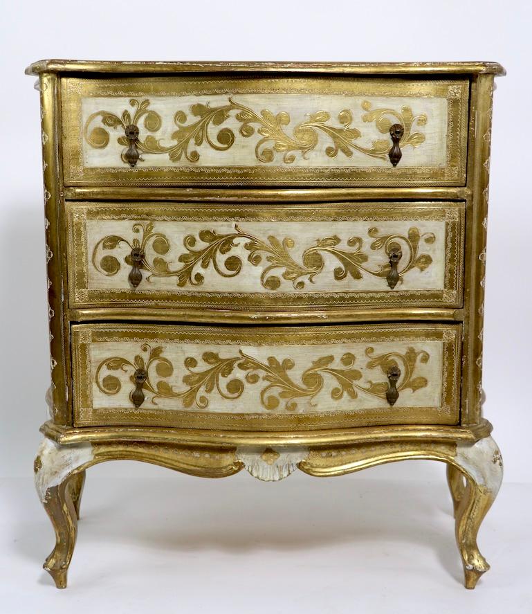 Diminutive three-drawer chest having decorative foliate gilt trim on an antique white ground. The case is shaped with Bombay sides and a serpentine front, making this chest even sexier. Made by Florentine Furniture, marked Made in Italy. Good,