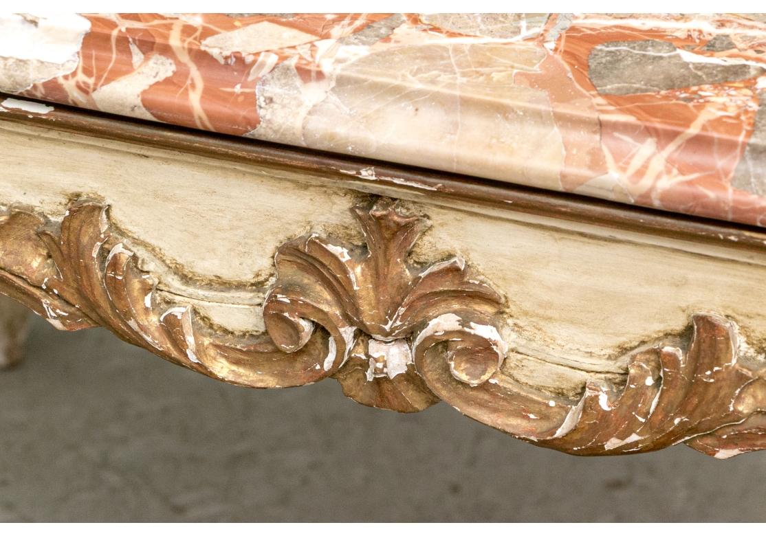 The base is carved wood with a gesso finish.  The table's design, with its ornate carvings, cabriole legs, and gilded highlights, is characteristic of historical European furniture featuring detailed carvings of motifs like shells, acanthus leaves