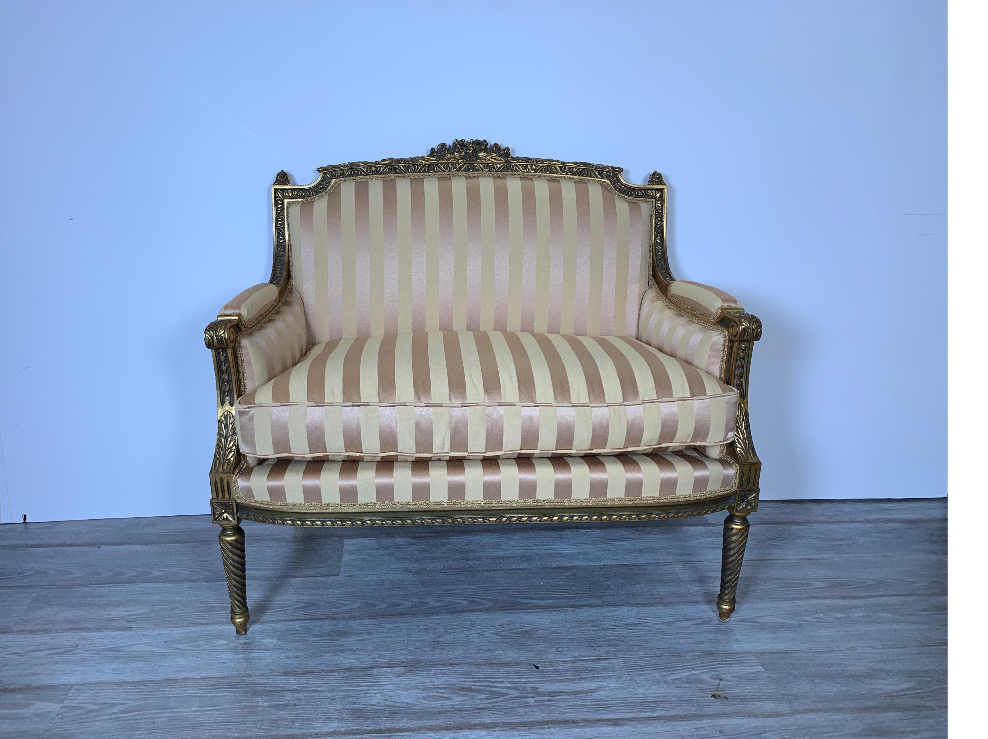 A diminutive giltwood settee in the Louis XVI style. The gold frame with carved detail all along the frame. The upholstery is newly covered in a soft gold beige satin stripe damask.