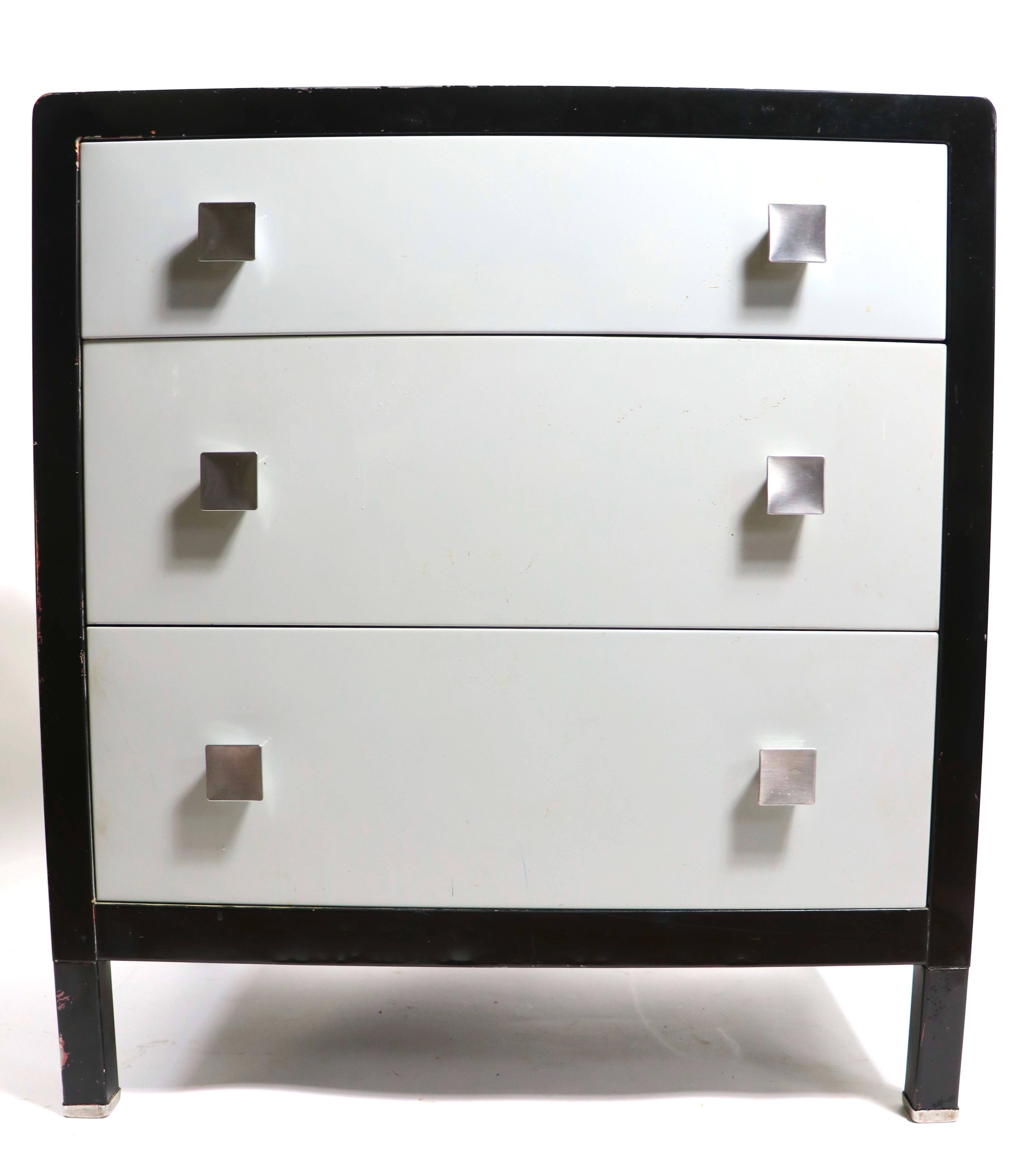 Coffre de célibataire sophistiqué de style Art déco, âge de la machine, conçu par Norman Bel Geddes pour Simmons Furniture. La commode présente une caisse noire, des tiroirs gris pâle, avec des poignées en métal brossé. Trois tiroirs, tous