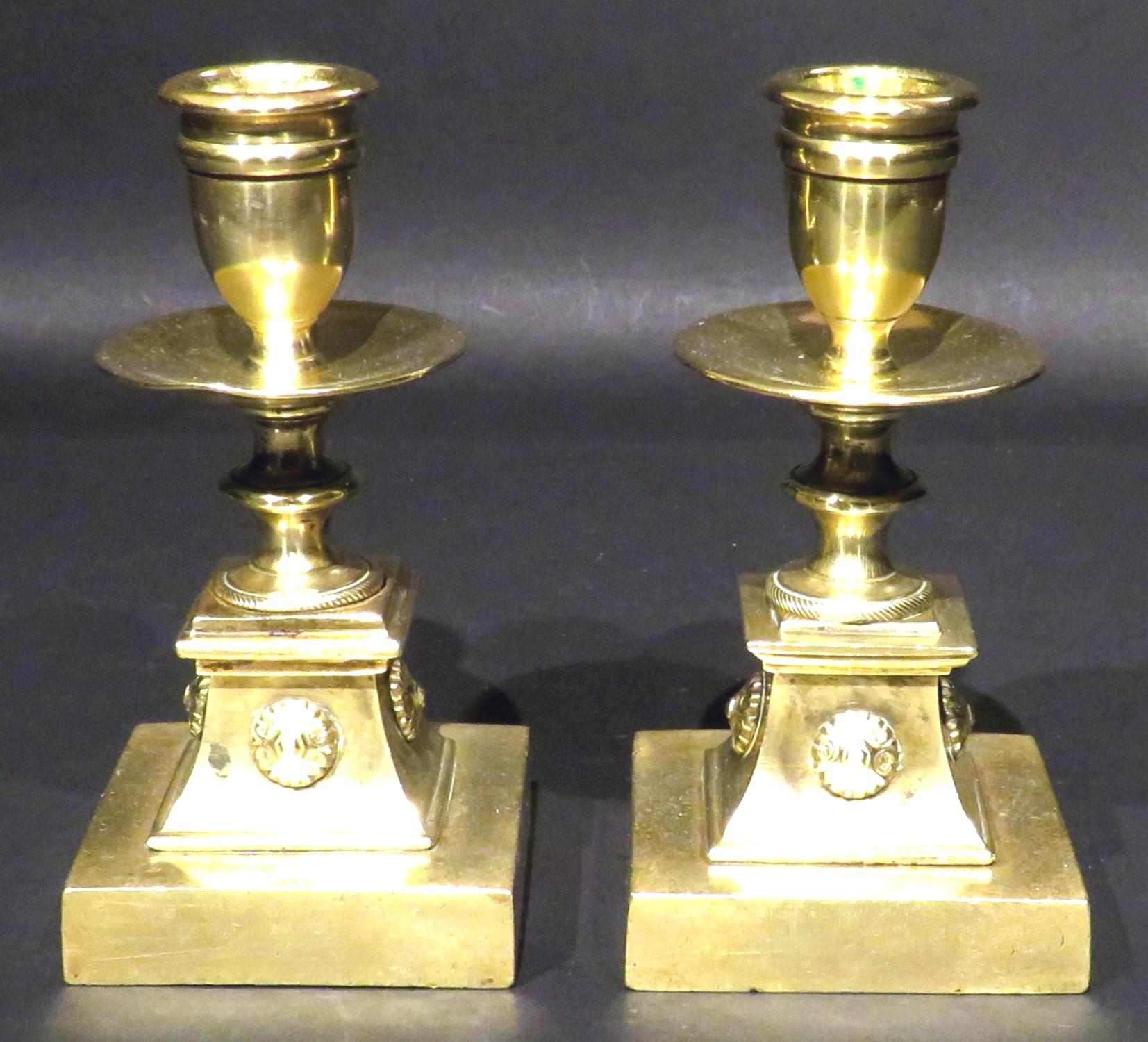 A very fine & diminutive pair of 19th century neoclassical gilt bronze dwarf candlesticks, showing urn shaped nozzles & flattened drip pans mounted atop turned columns rising from cavetto-shaped plinths on squared bases. 
All sections are
