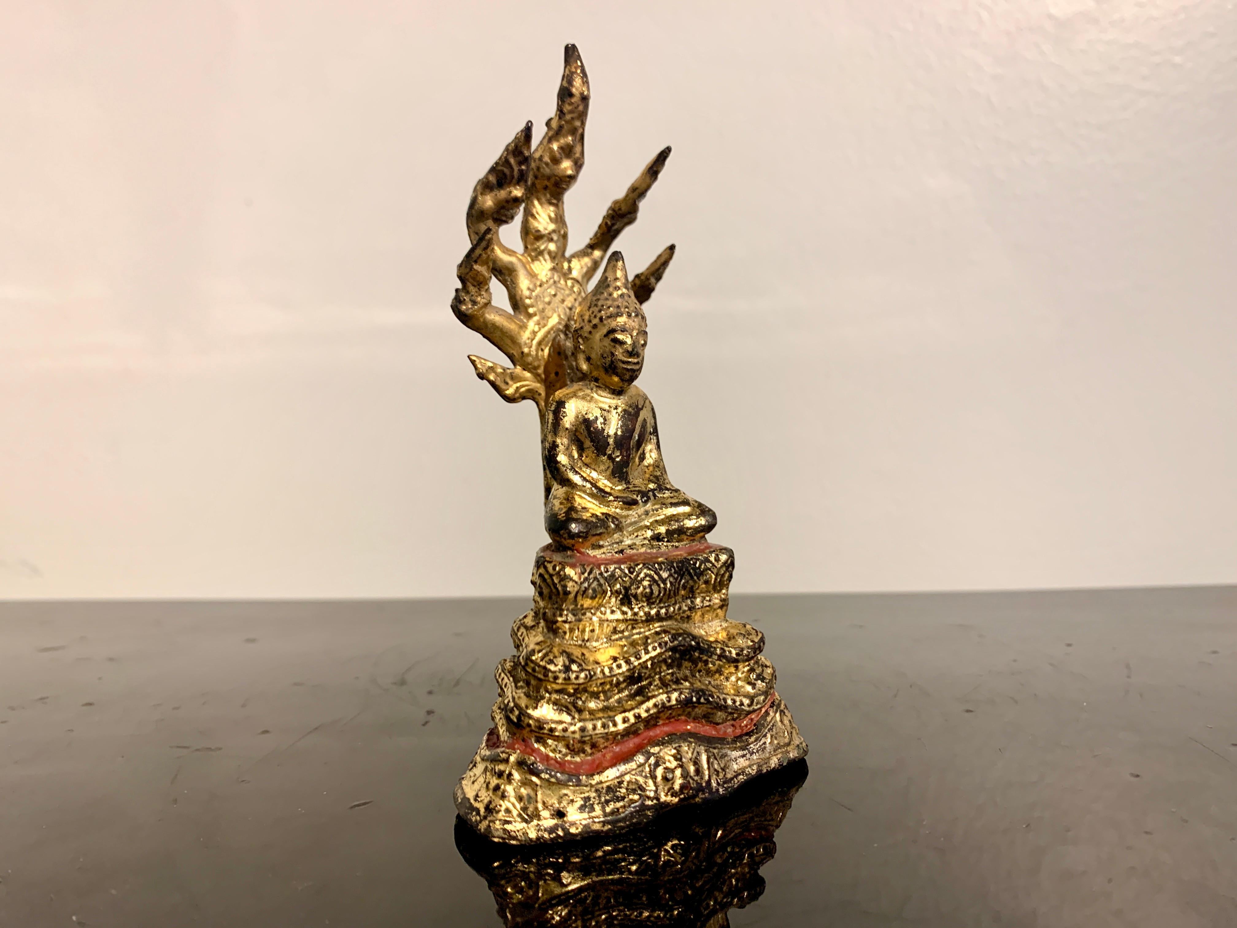 A small and charming Thai cast and gilt bronze figure of the Buddha sheltered by a Naga, Buddha Muchalinda, Rattanakosin Period, 19th century, Thailand.

This diminutive sculpture portrays the historical Buddha Shakyamuni in meditation. He is