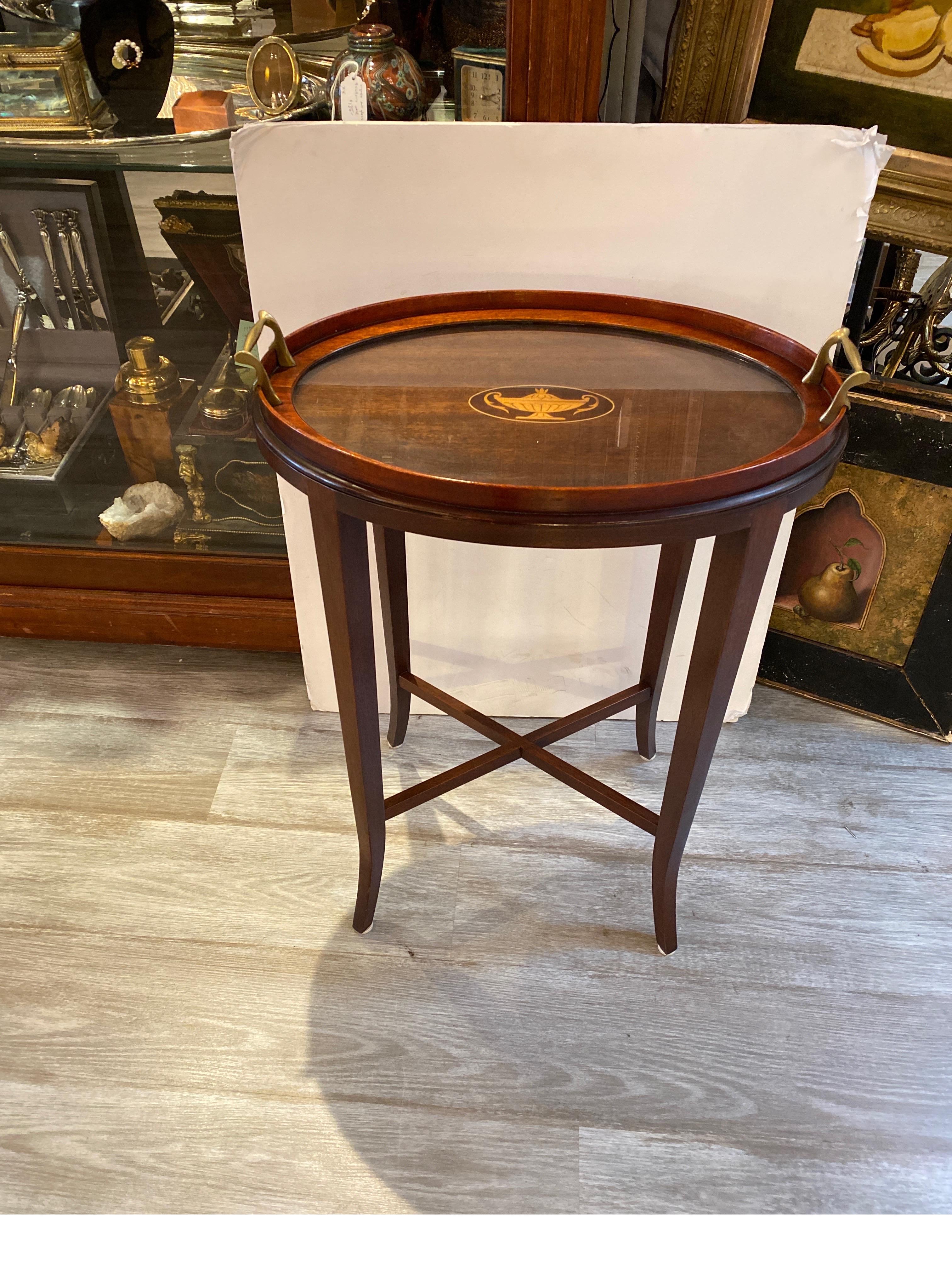 A diminutive tray top side table in mahogany with inlaid center. The removable fitted tray with brass handles and protective glass top. The later Custom base with Classic Hepplewhite style sabre legs. Measures: 19 wide, 13 deep, 26 high.