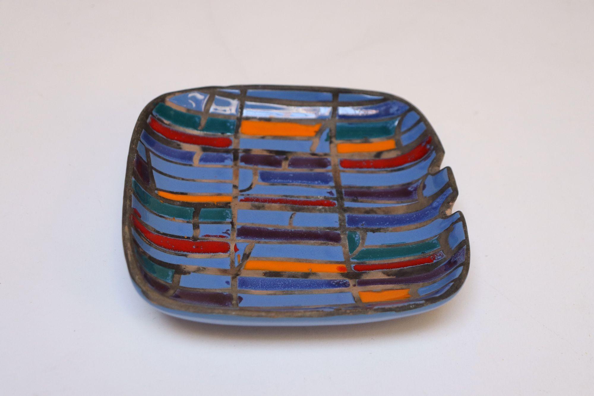 Posacenere piccolo di Raymor con motivi di pervinca, blu, arancione e rosso su una base non smaltata che sembra quasi un Boi (circa anni '60, Italia).
Alcuni dei rettangoli sono incompleti per design, dando al disegno un'estetica astratta.
Un pezzo