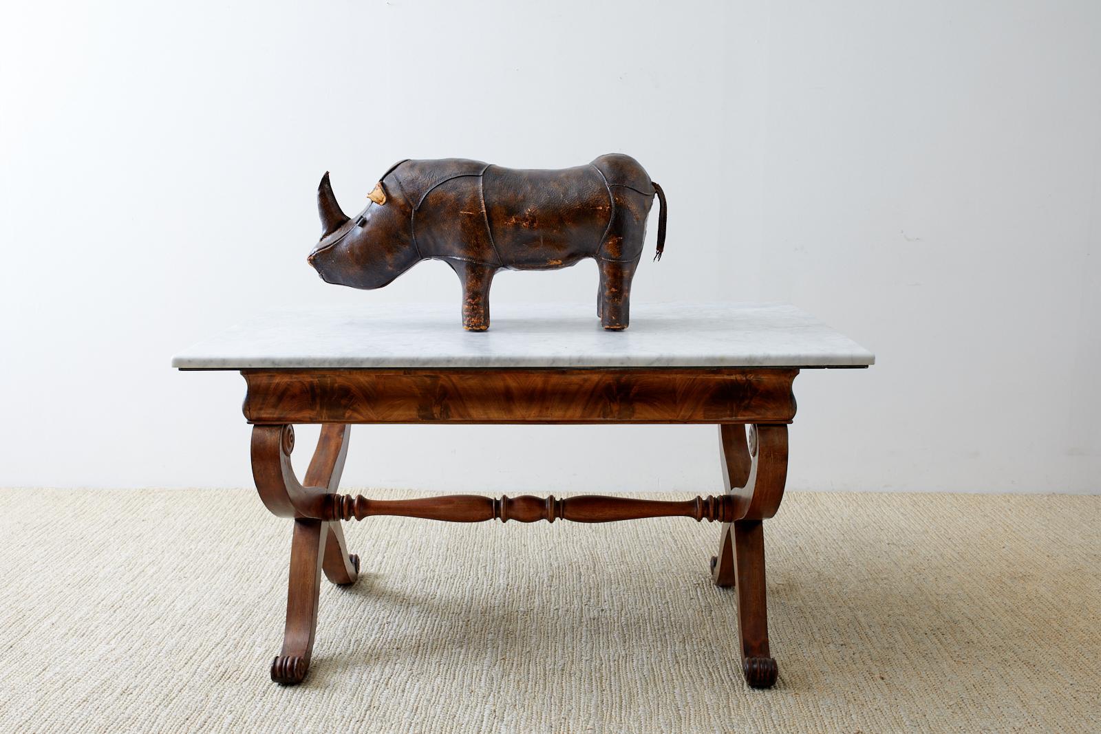 Mid-century English leather footstool in the shape of a rhino designed by Dimitri Omersa for Abercrombie and Fitch. Good solid construction with a beautifully aged patina on the thick leather. Intact with all eyes, ears, horn, and tail. From an