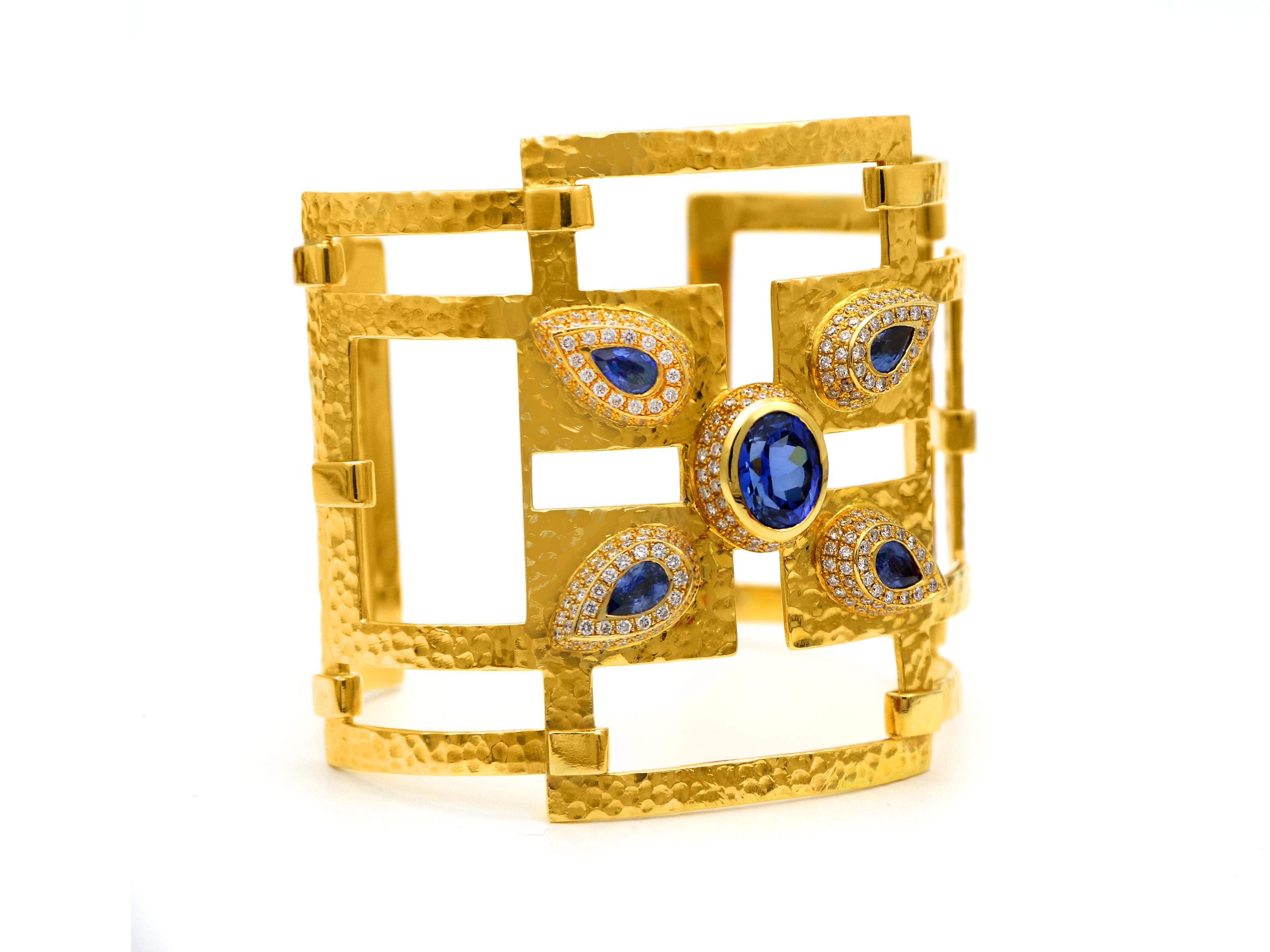 Geometrical inspired bracelet married with a hummer gold workmanship and the attitude of an edgy style. Hosting an oval 4.95 carats Tanzanite and 4  teardrop 1.18 carats Ceylon sapphires. A very wide bangle bracelet with a beautiful finish a