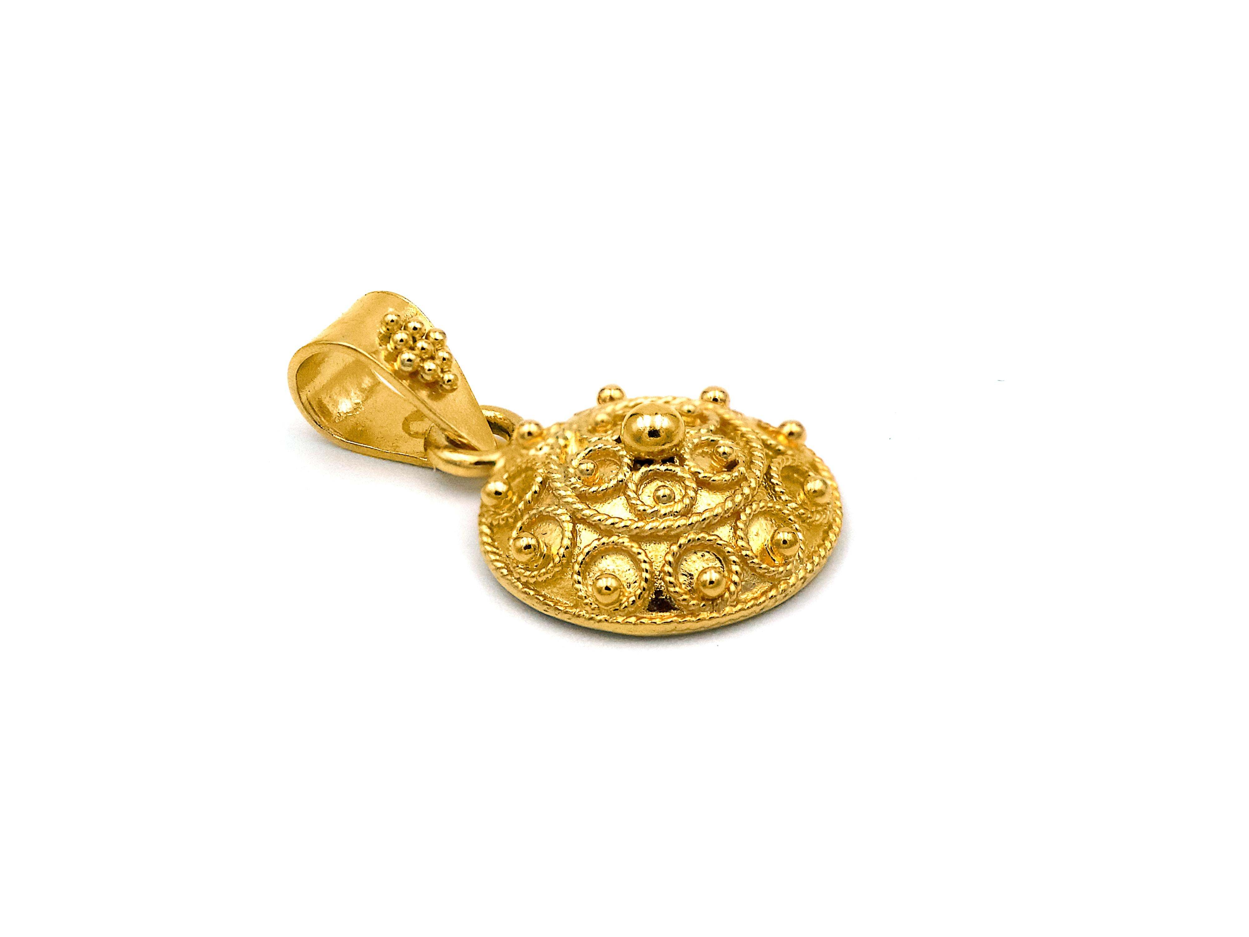 Le pendentif Bocola est serti dans de l'or jaune 22k. Le motif est créé avec des cercles de filigrane et des granulations de différentes tailles tout autour. Le cerceau est simple et épuré, de sorte que l'accent reste sur le pendentif.