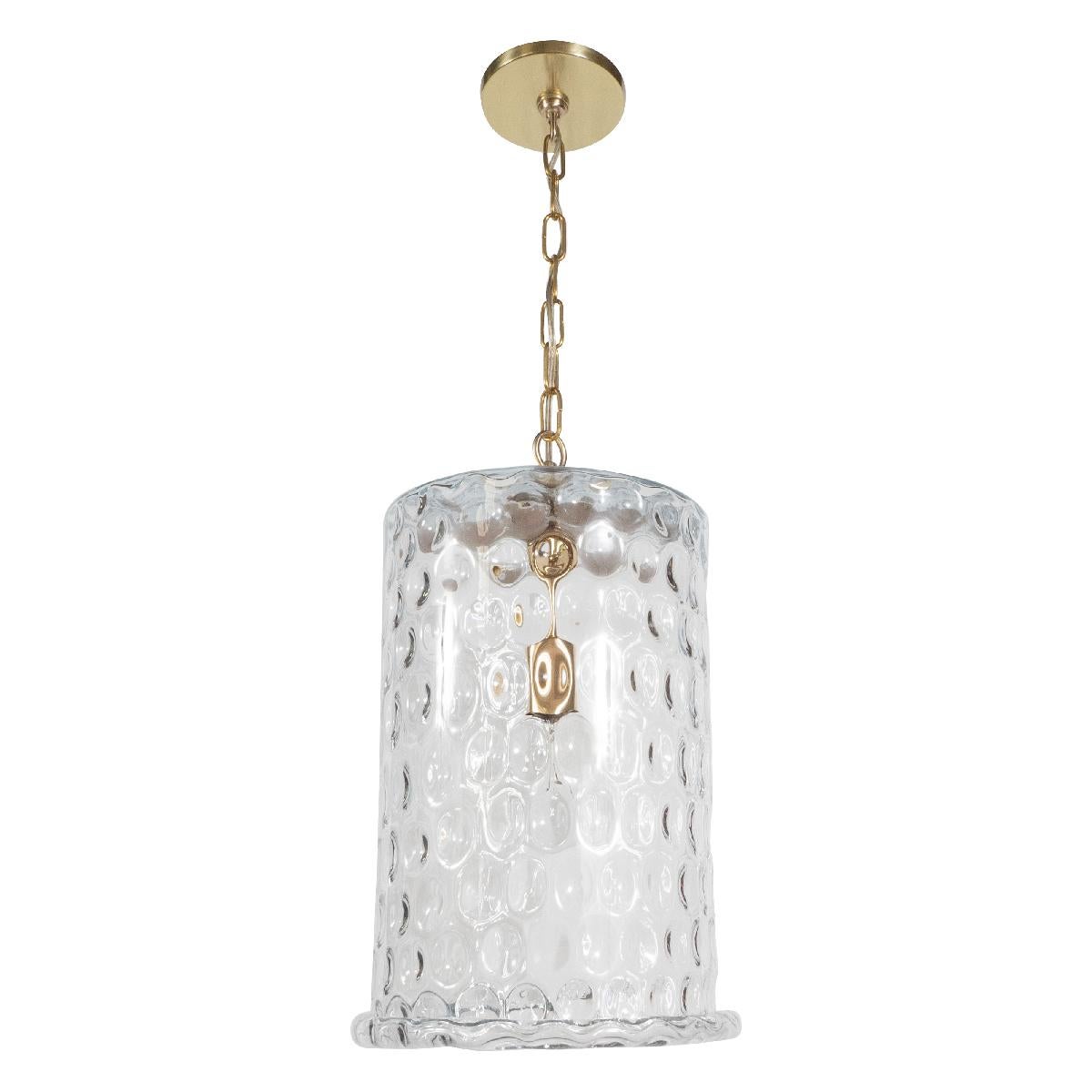 Mid-Century style pendant ceiling fixture composed of a cylindrical dimpled glass shade with brass hardware by Spark Interior. Measured without chain. Additional quantities can be made to order.