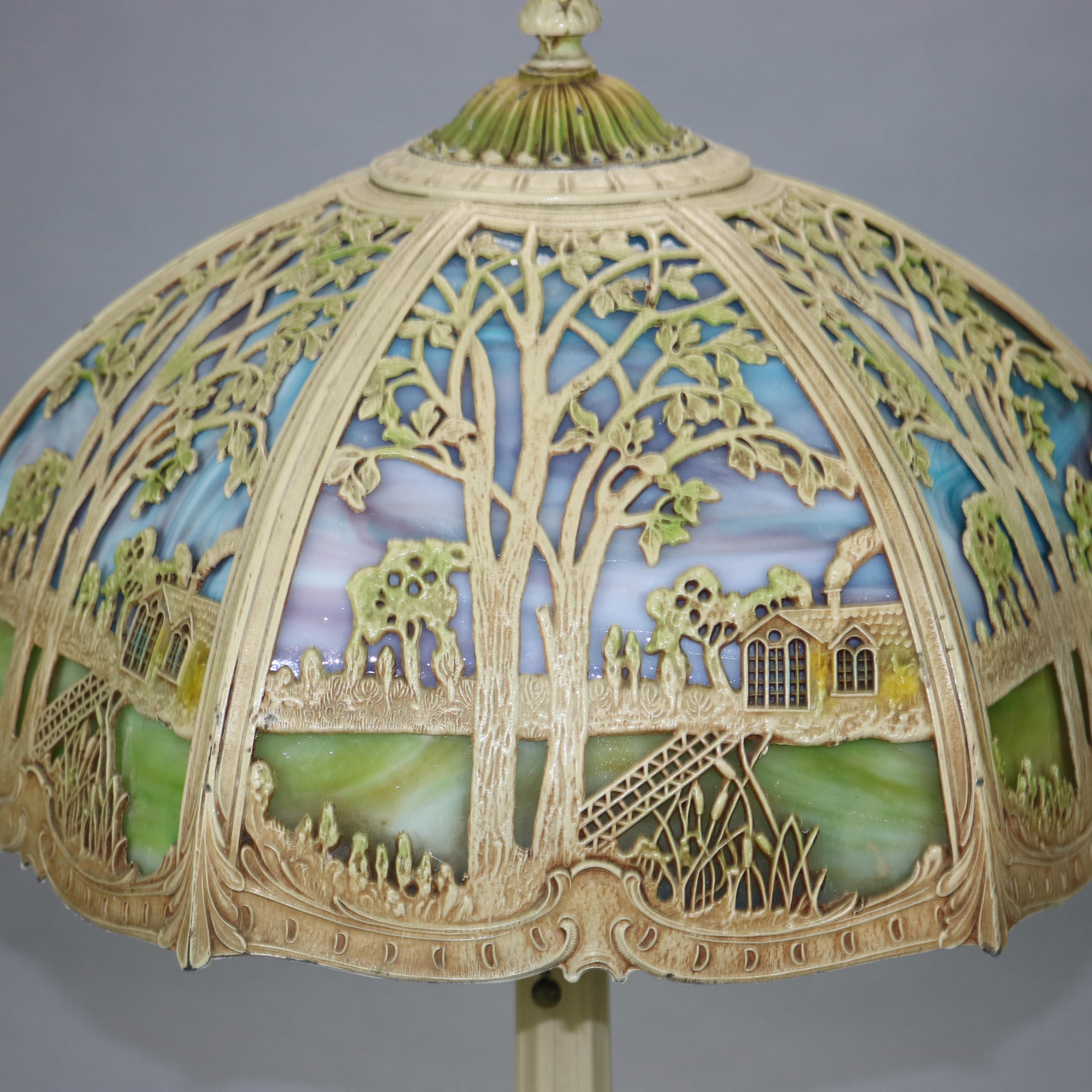 An antique Arts and Crafts table lamp in the manner of Miller offers filigree overlay domed shade with landscape scene and housing polychrome slag glass over double socket base, c1920

Measures: 22