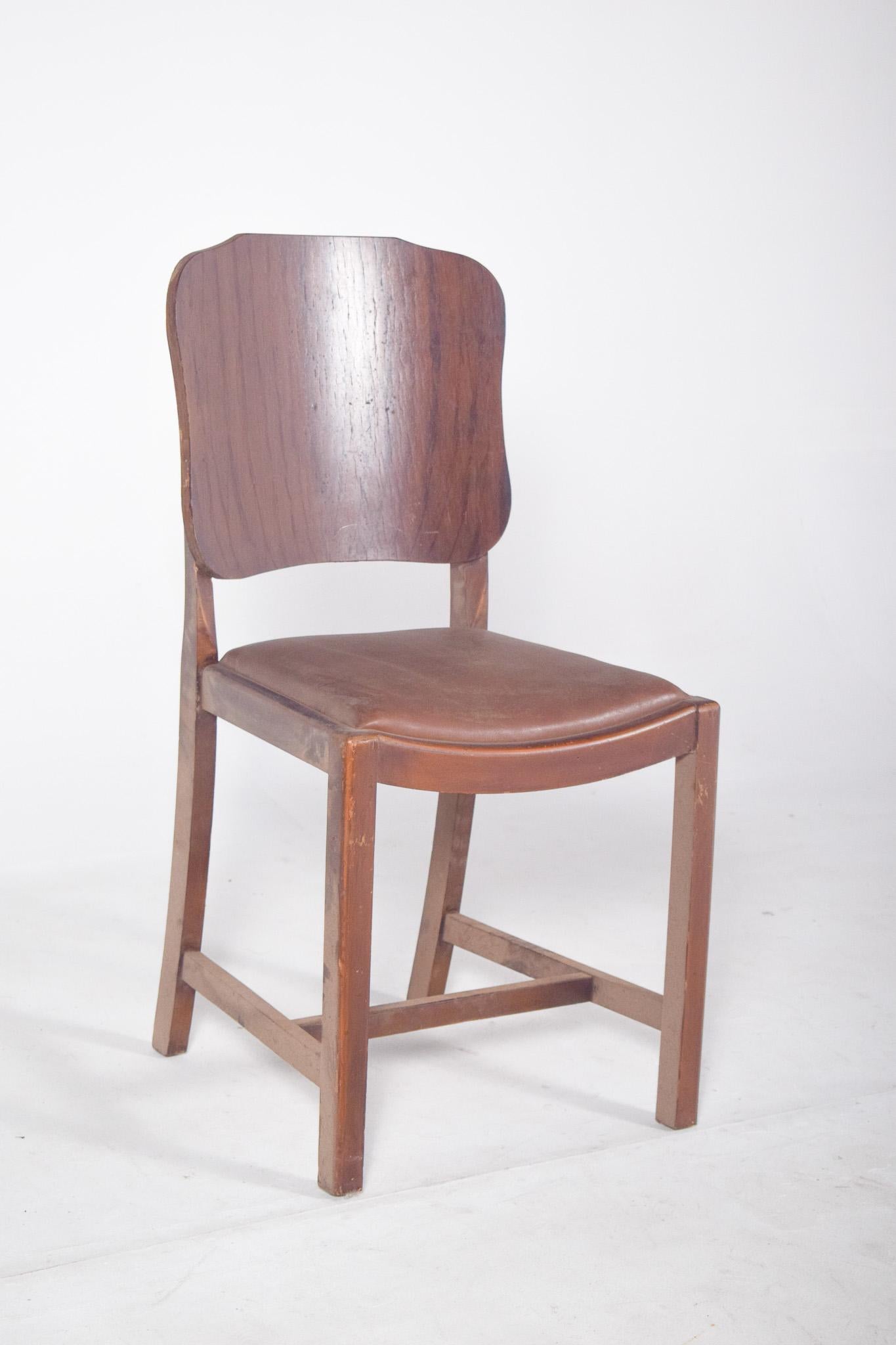 Chair with rounded corners backrest.  Wooden chair with molded plywood backrest and seat upholstered in brown synthetic material, the backrest has a slightly cut-out shape on the sides and features visible wood grain. The seat, upholstered and