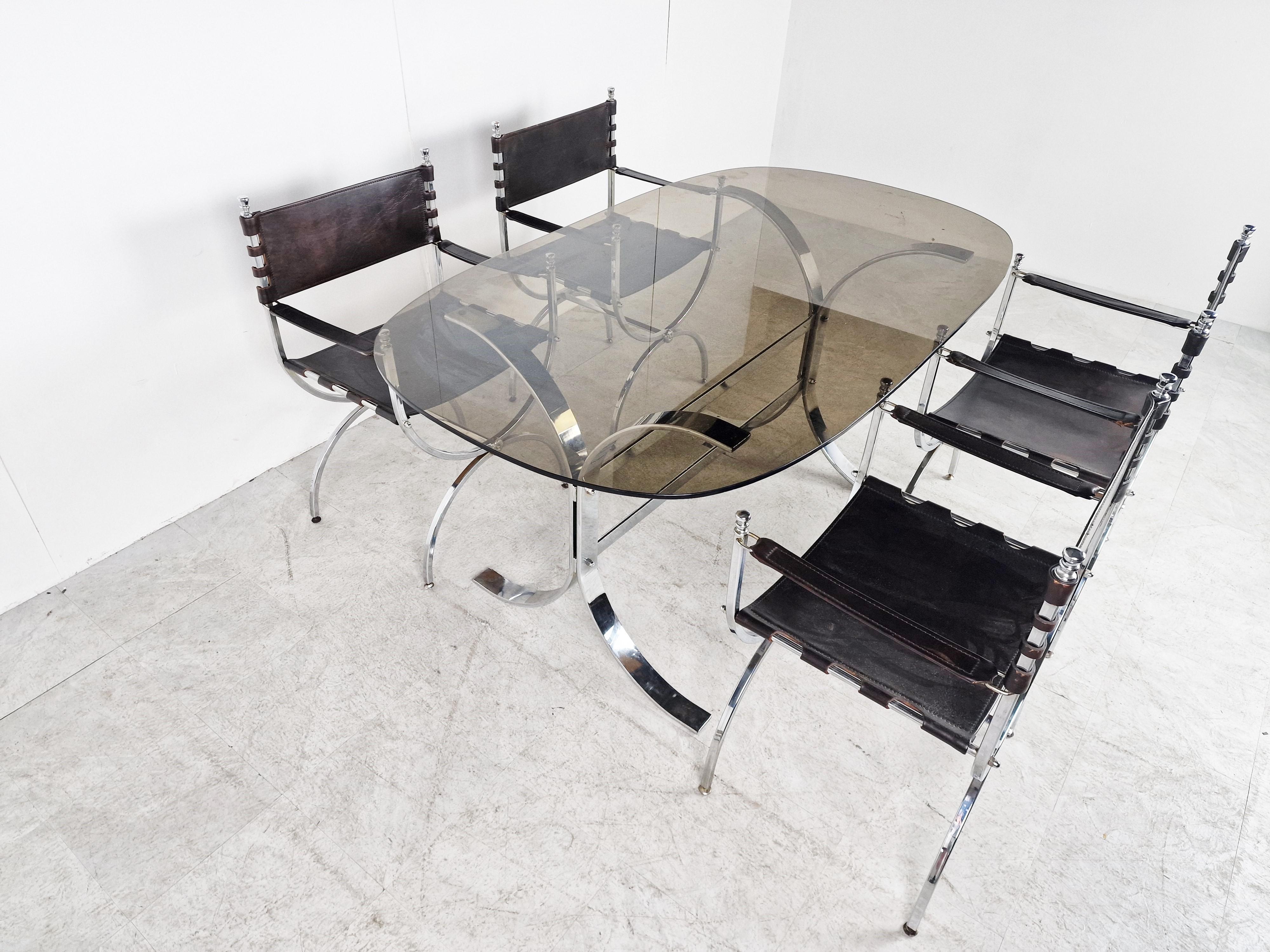 Luxurious dining chairs by Maison Jansen with matching table.

The chairs have a heavy steel frame and strong brown sling leather seats, backrests and armrests.

The table has a chromed steel frame and a smoked glass top.

The chairs are of a
