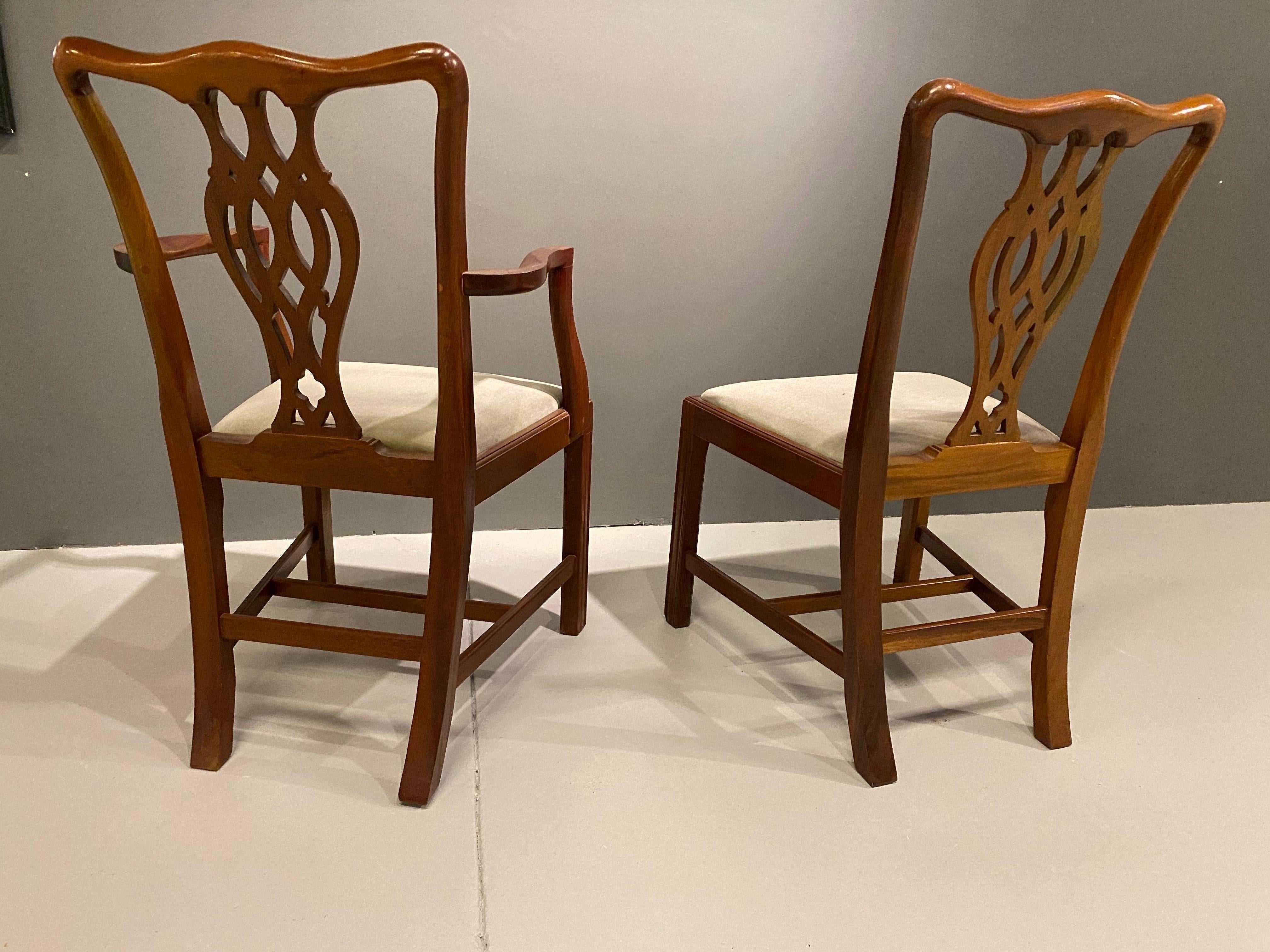 A solid set of eight Georgian style mahogany dining chairs made in England. The Chippendale style chairs are a set of eight made up of two chairs with arms and six without arms. Upholstered in their original mint green cover with the pop out seats