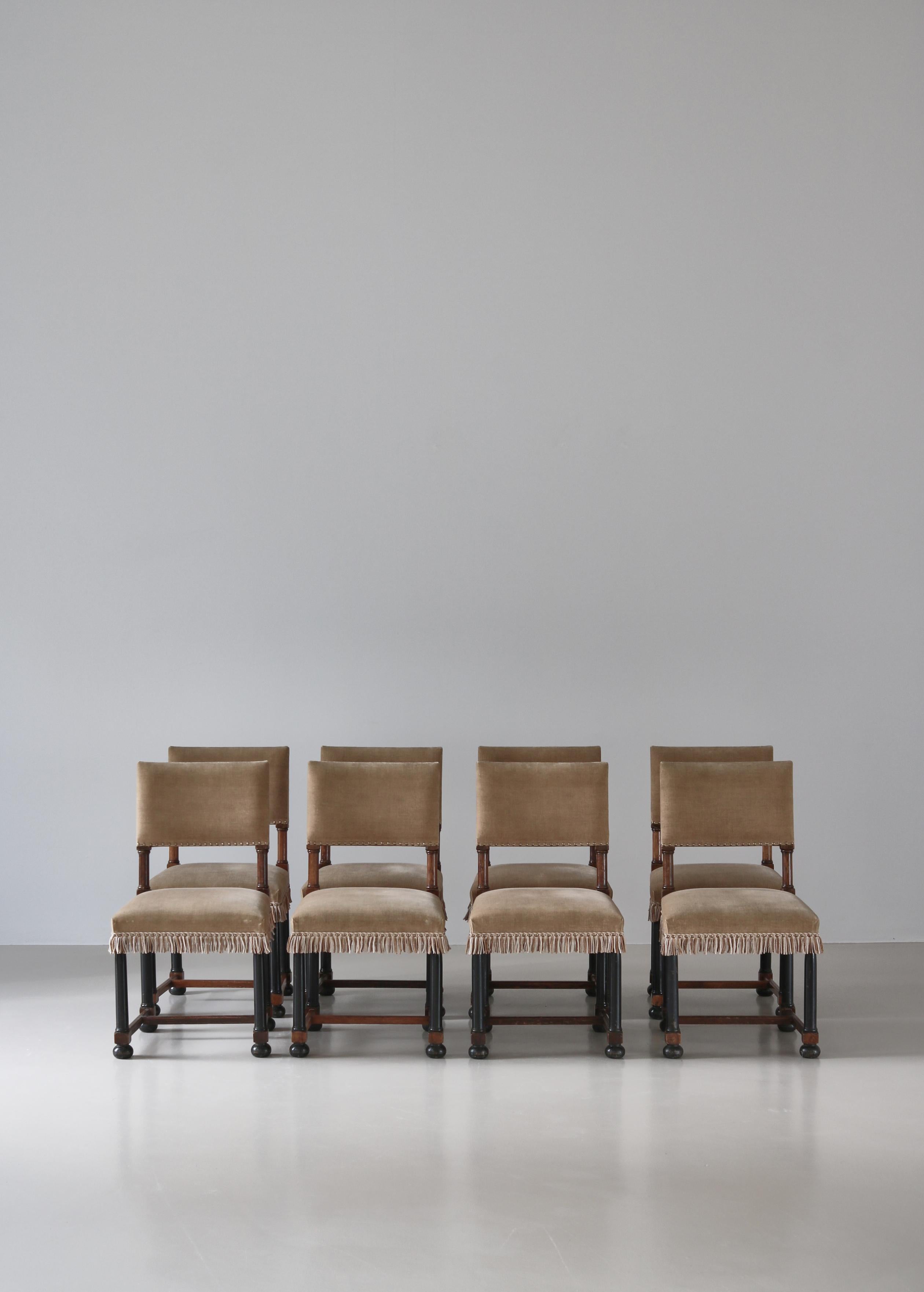 A stunning set of 8 Swedish Grace dining chairs in the style of Axel-Einar Hjorth. Made in Sweden in the 1920s in solid oak with original black lacquer. The chairs are upholstered in beige velvet with decorative fringes and nails.

British