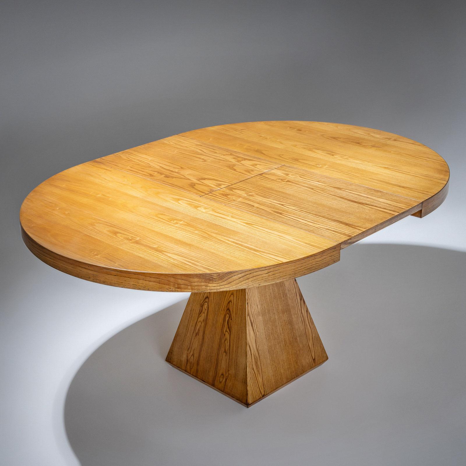 Ausziehbarer Tisch aus hellem Eschenholz mit runder Tischplatte und pyramidenförmigem Fuß. Die elegante, minimalistische Formensprache ist auf geometrische Grundformen reduziert und bringt die feine Materialität des verwendeten Holzes voll zur