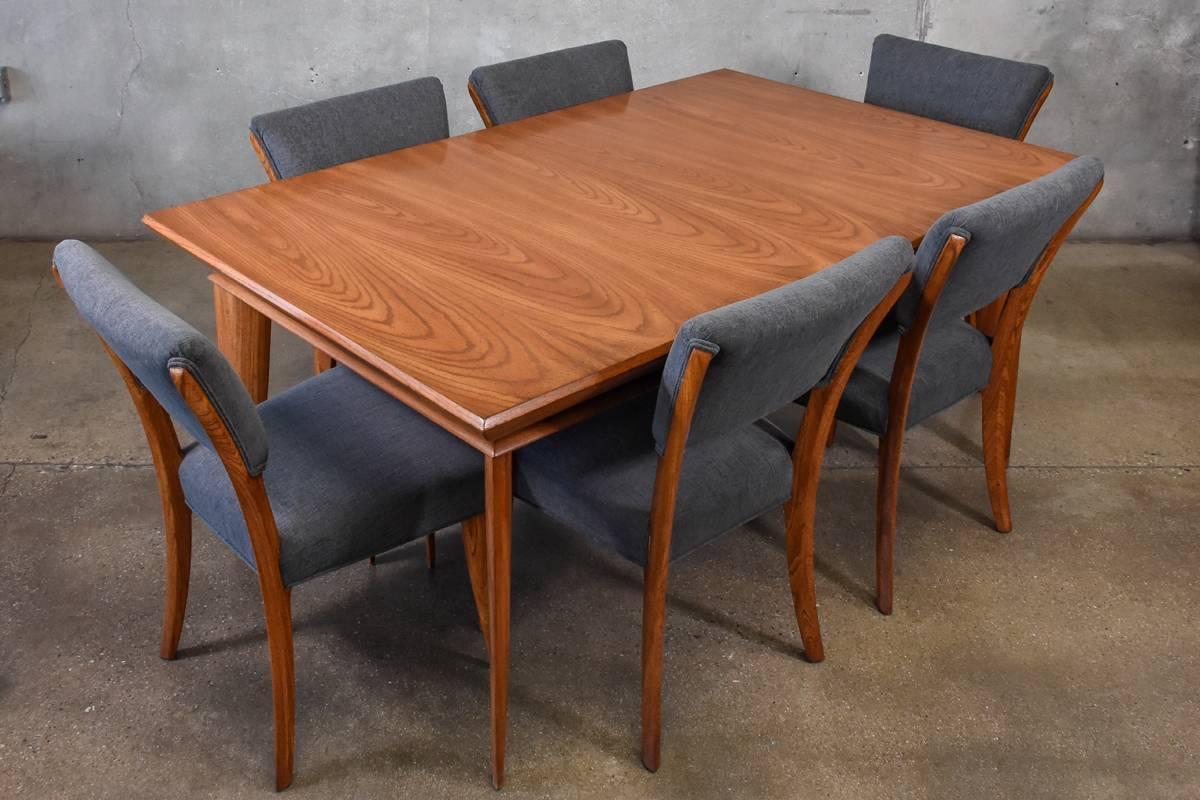 An angular oak dining table with six chairs designed by Paul Laszlo for Brown Saltman. The table can expand with two 15 inch leaves, allowing the table to seat up to ten. The chairs have been reupholstered in a neutral grey fabric. The table and