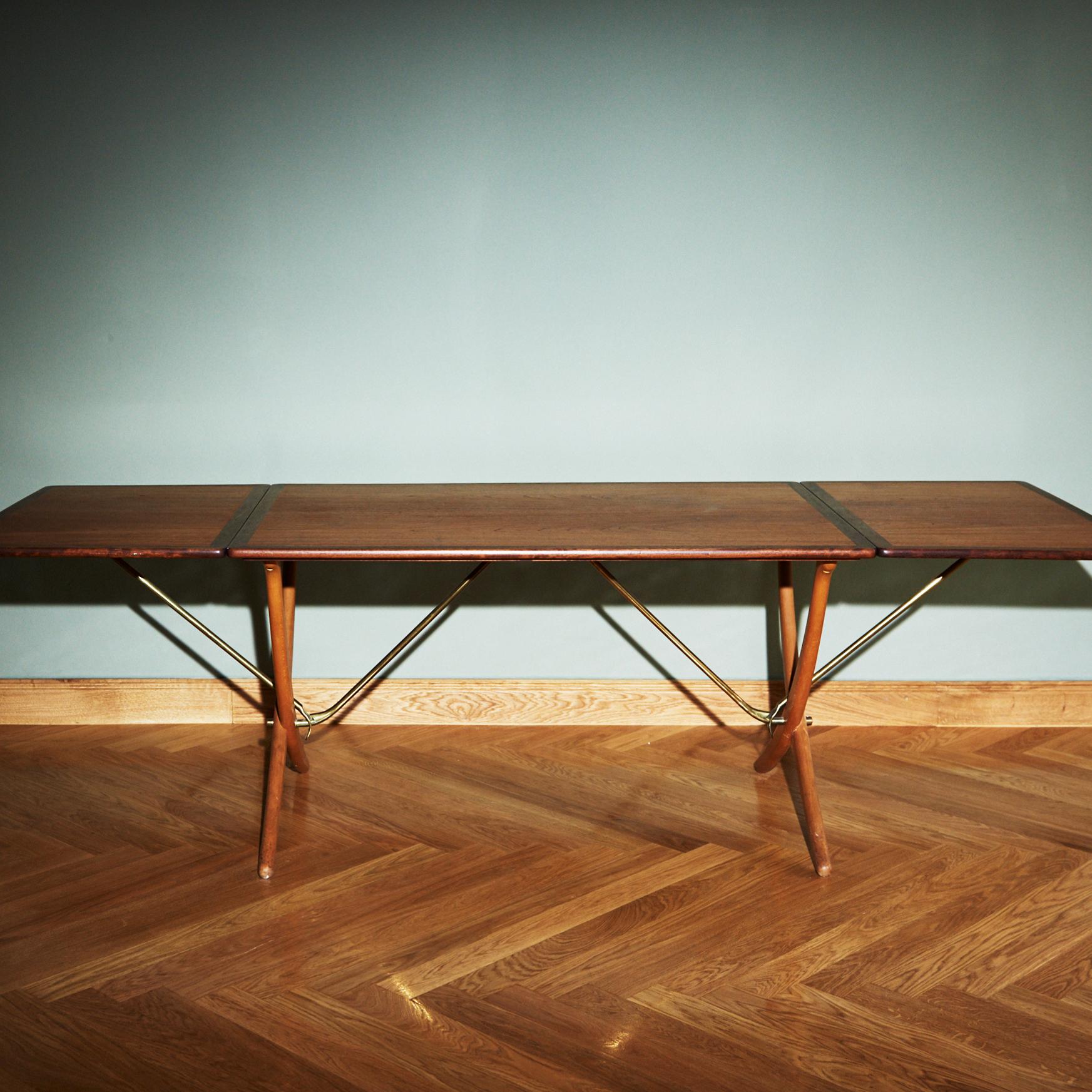 Table de salle à manger produite par Andreas Beeche avec un plateau rectangulaire en teck qui peut être prolongé sur les côtés et des pieds en bois de hêtre courbés et croisés avec des joints en laiton.