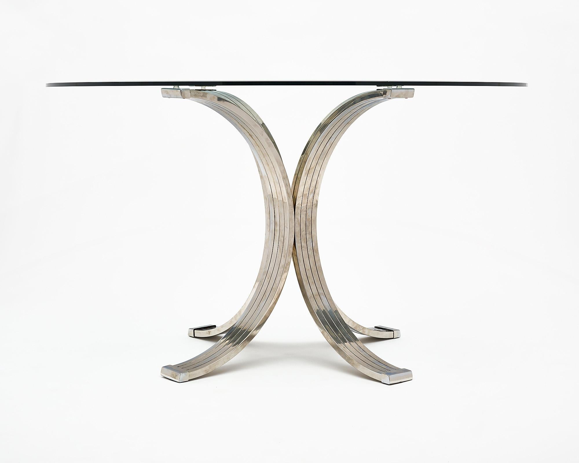 Table ronde, d'origine italienne, attribuée au designer emblématique Romeo Rega. Cette table est dotée d'un plateau en verre avec biseau et d'une base comportant quatre éléments arqués en laiton et en acier chromé.
