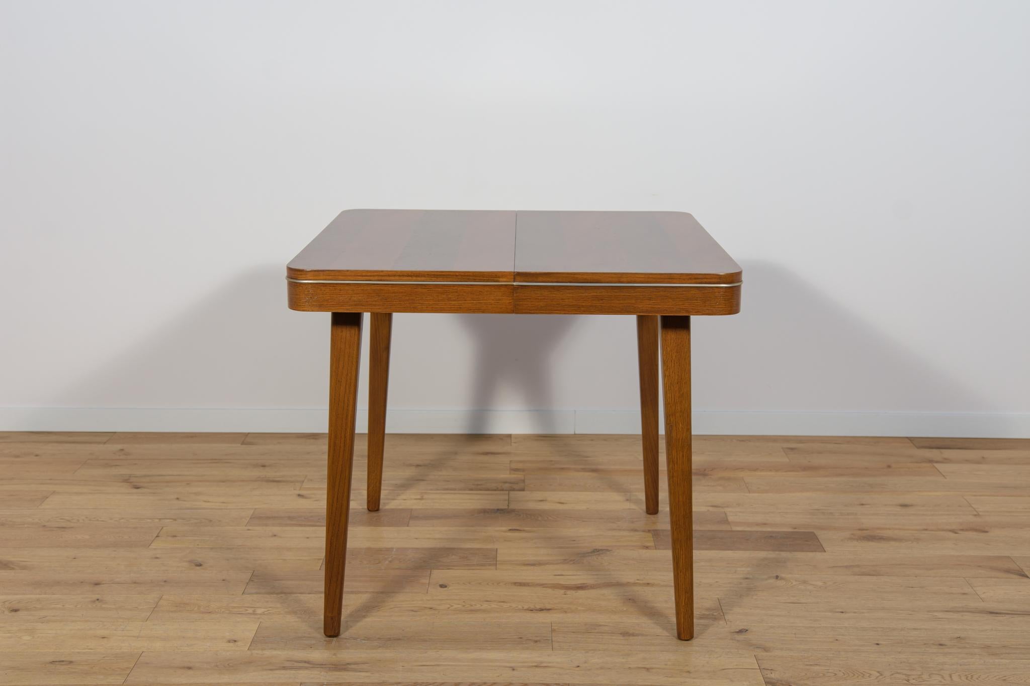 The dining table was designed in the 1950s by Bohumil Landsman and Hubert Nepozitek. It was produced in the 1960s by the Jitona Soběslav furniture factory in Czechoslovakia. Legs made of oak wood, top made of walnut wood. It has golden, aluminum