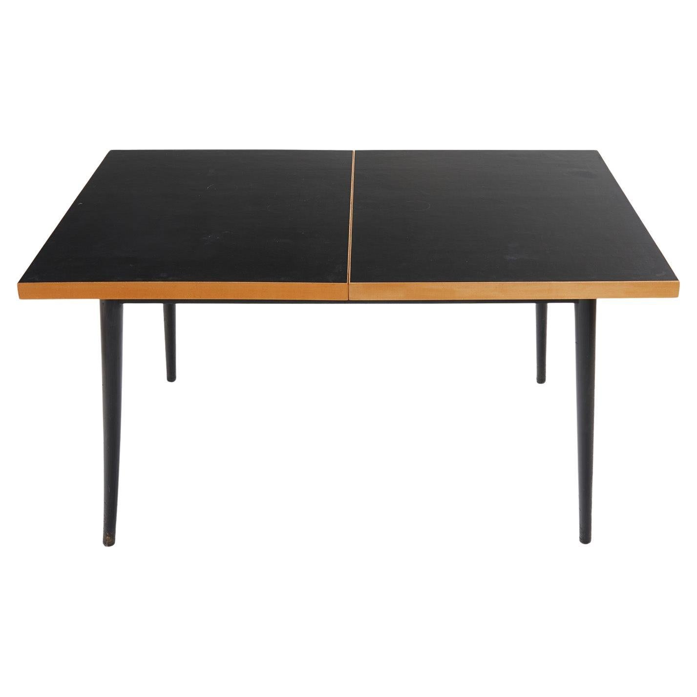 1955 entwarf der Schweizer Designer Fred Ruf diesen minimalistischen Esstisch für Wohnbedarf Schweiz.

Dank einer Verlängerungsplatte, die zwischen die beiden Platten passt, kann der Tisch von 140 cm auf 200 cm verlängert werden. 

Die hölzerne
