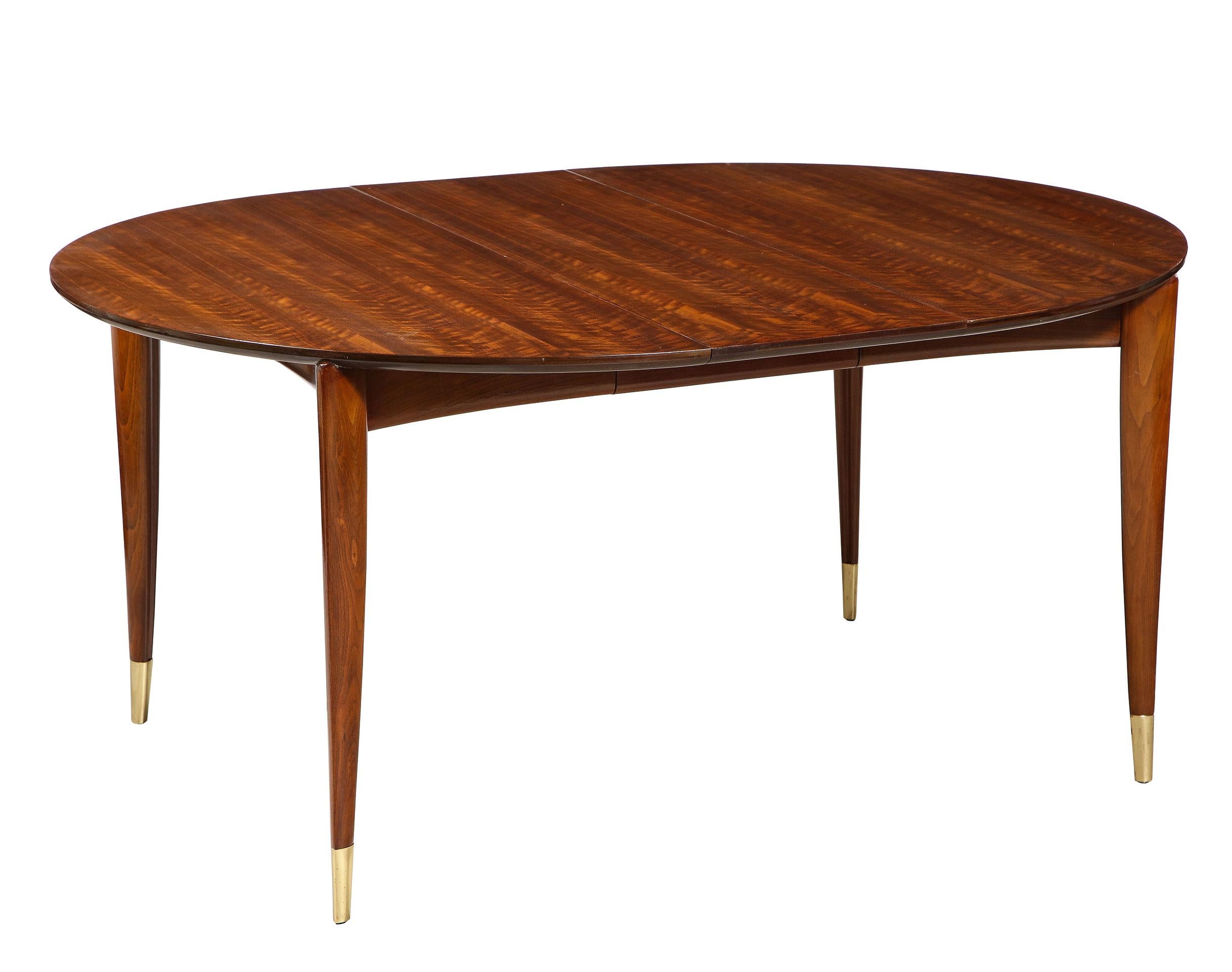 Having a lovely lacquer finish, the walnut dining table for M. Singer and Sons, starts as a round breakfast size table and expands to accommodate 10-12 chairs. The lovely grained top over a slightly concave apron. With 4 tapered legs with brass