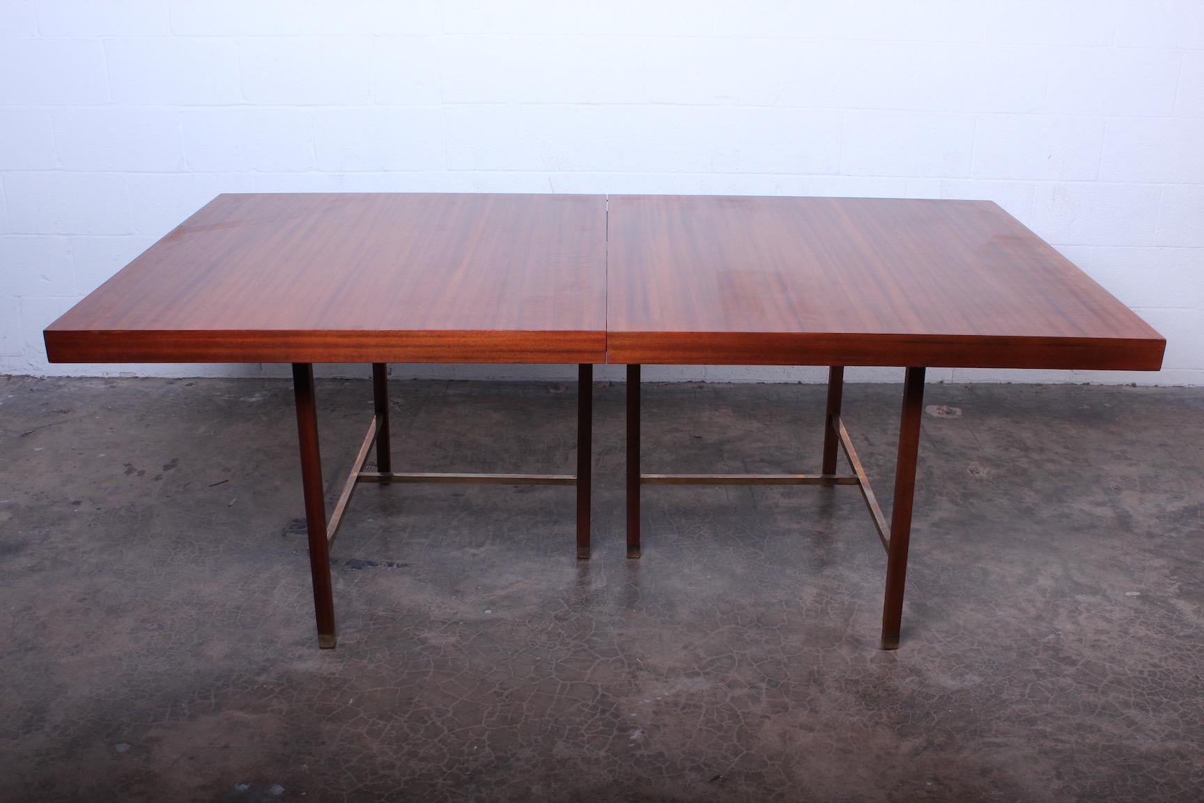 A large mahogany dining table on mahogany base with brass stretchers. Designed by Harvey Probber. Measures: 112