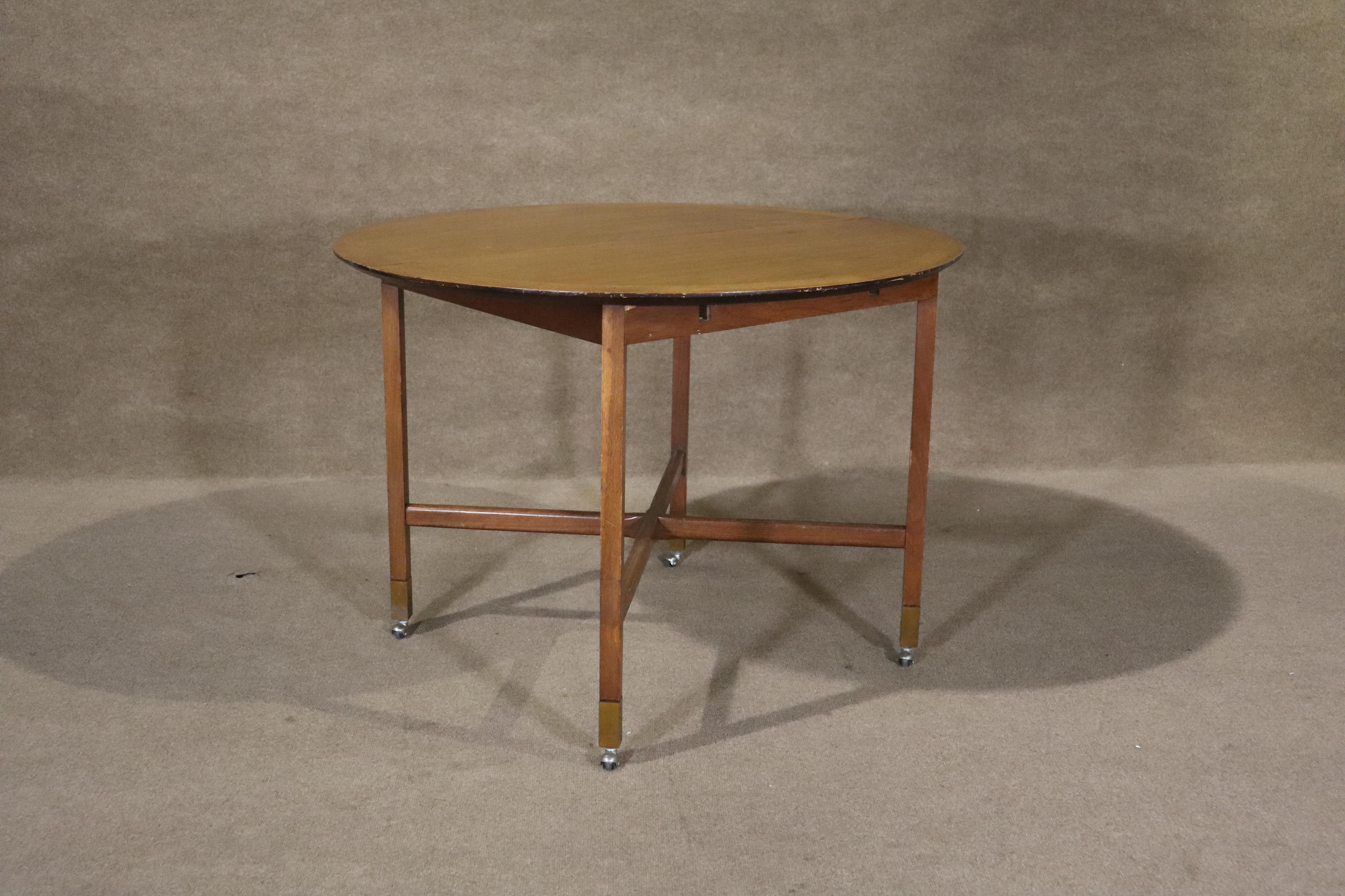 Round dinette table by Founders on caster wheels. Simple round design with cross stretchers and brass caps. Opens to accommodate leaves.