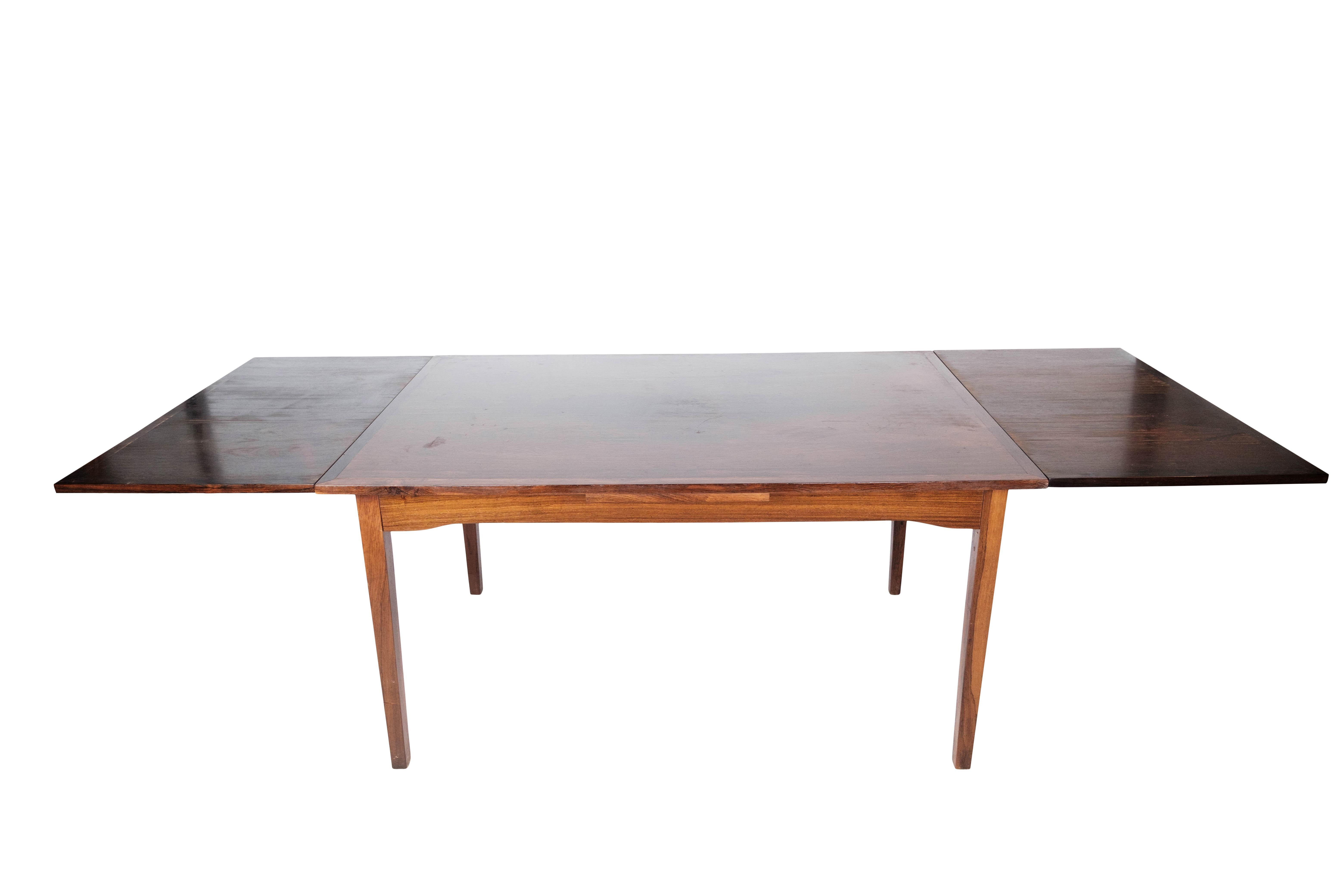 This 1960s rosewood dining table is a beautiful and functional addition to any dining room. With its simple design and pull-out function, it offers extra space for your guests when needed.

Behind this table stands Ellegaards Møbelfabrik, a