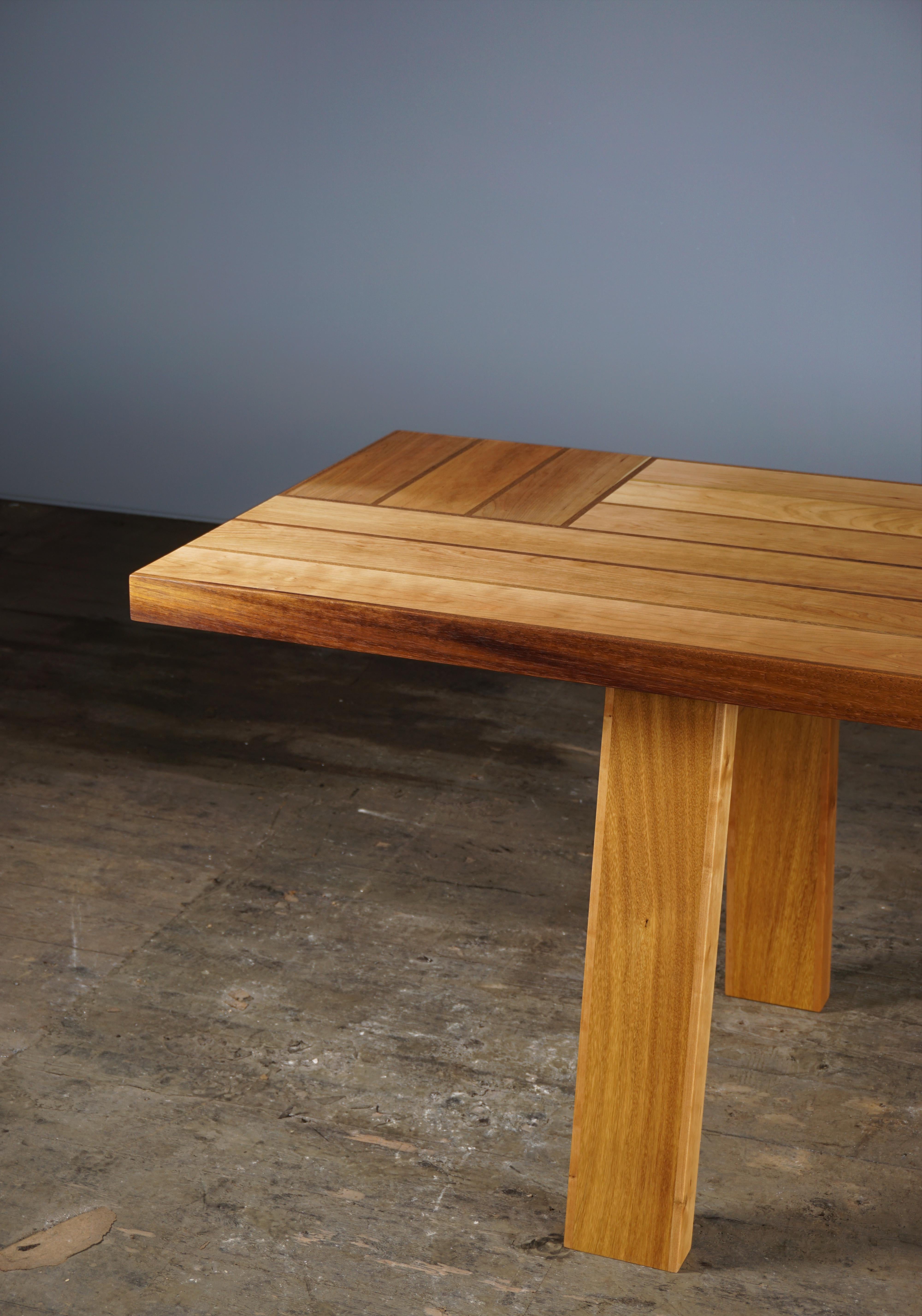 This 11ft dining table is made of American Cherry and Iroko. 
The structure is inspired by the structural rigidity of an I-beam. The tabletop consists of a sequence of vertical and horizontal boards which results in an entirely hollow structure.