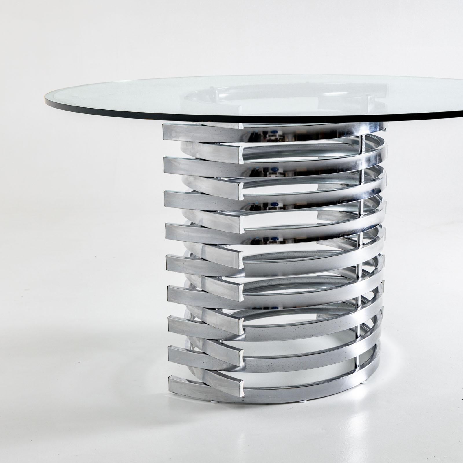 Grande table de salle à manger moderne avec structure chromée en arcs emboîtés et plateau rond d'un diamètre de 130 cm.