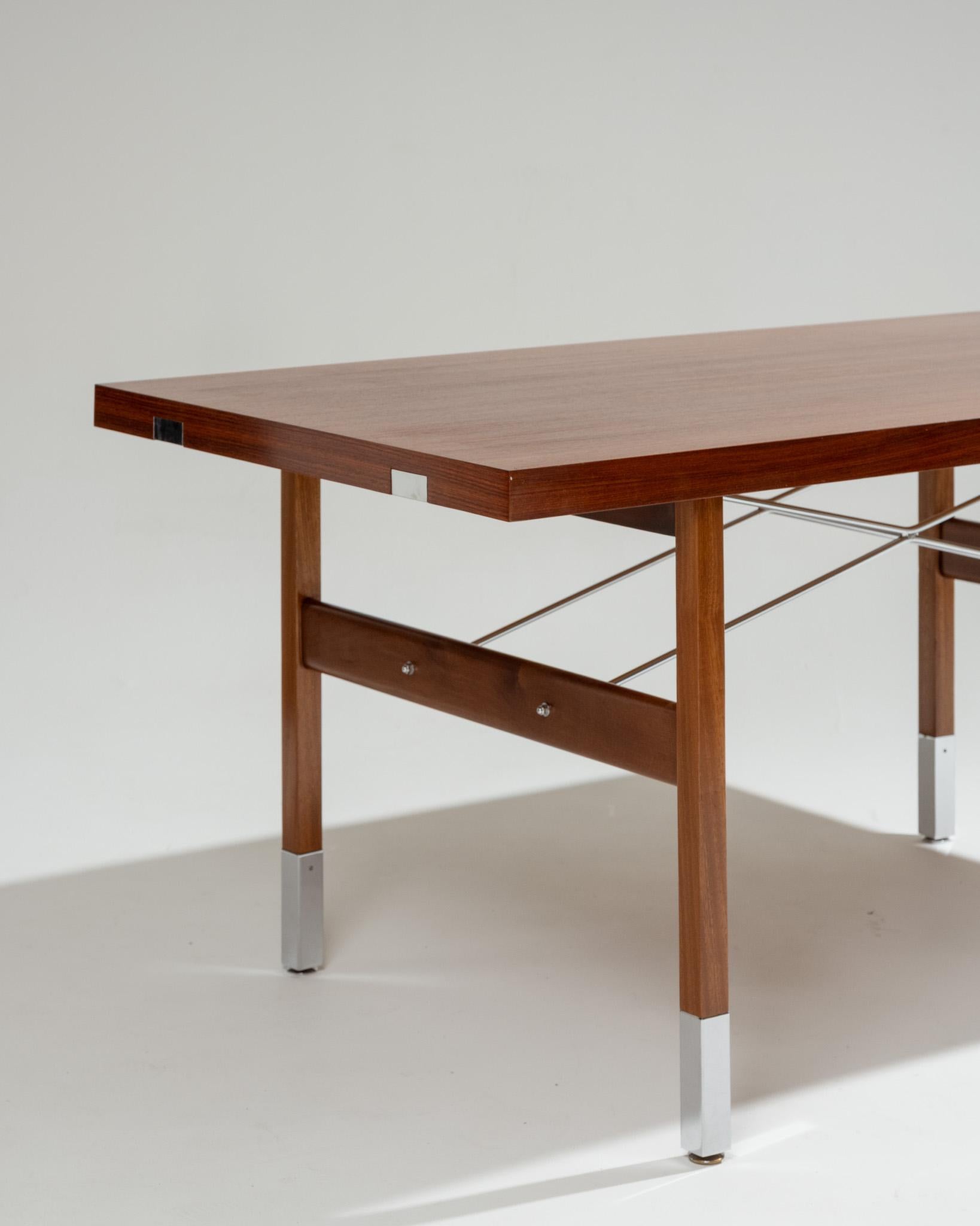 Table de salle à manger vintage des années 1950, signée Robert Debiève et éditée par Huchers Minvielle. Plateau rectangulaire en palissandre des Indes, reposant sur un piètement assorti avec sections chromées et patins réglables en hauteur. Les