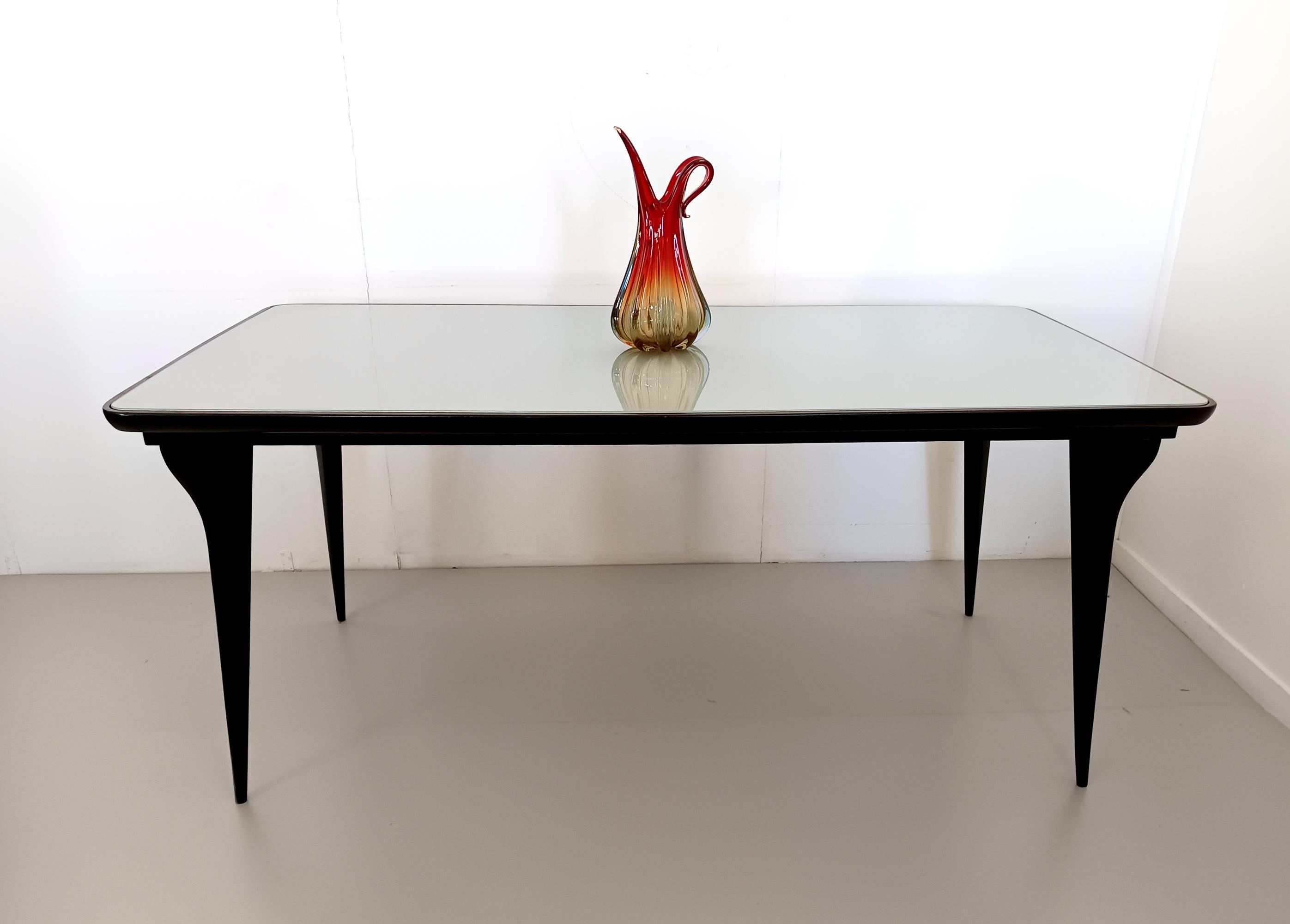 Fabriqué en Italie, années 1950.
Cette table de salle à manger présente un cadre en hêtre ébonisé et un plateau en verre vert pâle peint à l'arrière. 
Il s'agit d'une pièce d'époque, qui peut donc présenter de légères traces d'utilisation, mais qui