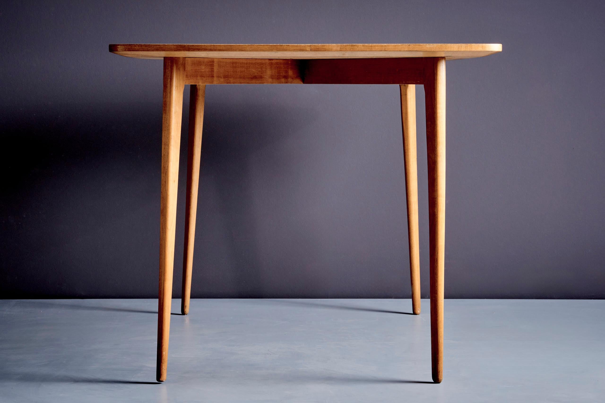 Dining table with ash veneer top with rounded edges and tapered legs. Vintage condition with minor wear consistent with age.


