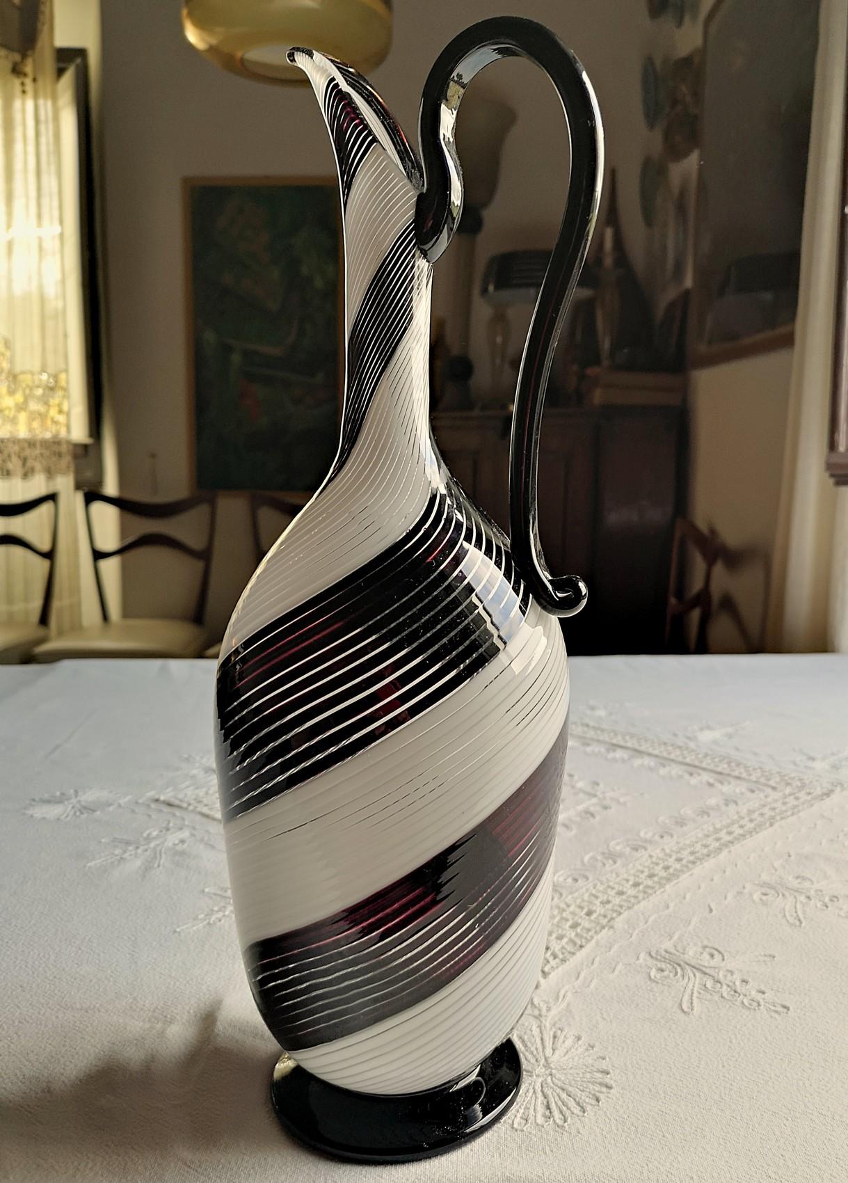 Sculptural pitcher from Dino Martens. There are 4 bands each with 12 filigrees alternated in white and black.
Black is not made with smalto technique, which was developed later by Effetre International and Lino Tagliapietra. This black is done in