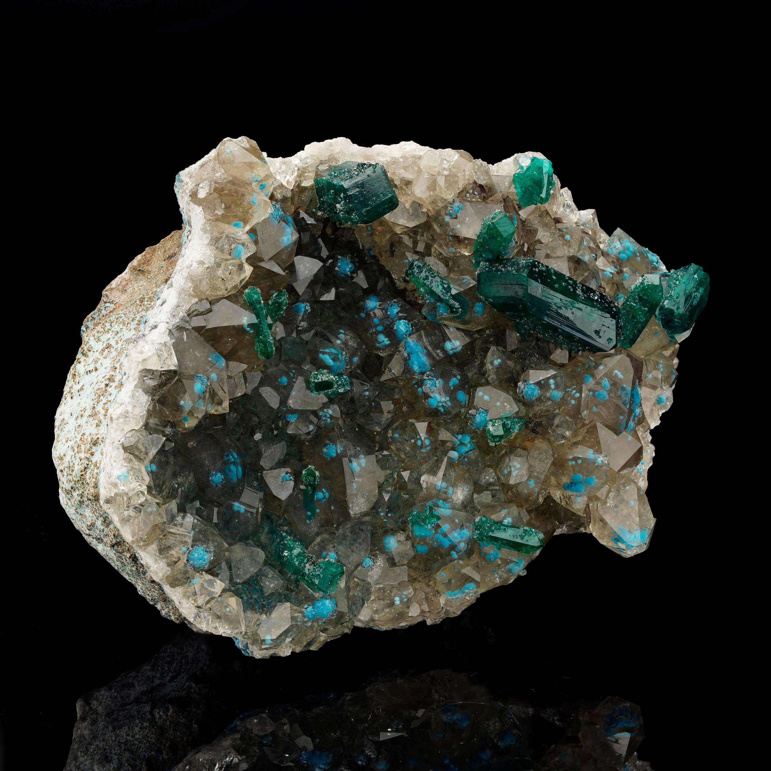 Questo esemplare dal contrasto vibrante mostra cristalli di diottasio verde smeraldo di dimensioni moderate che coronano una matrice di calcite cristallizzata, accentuata da rare formazioni di plancheite blu polvere che si mostrano vividamente