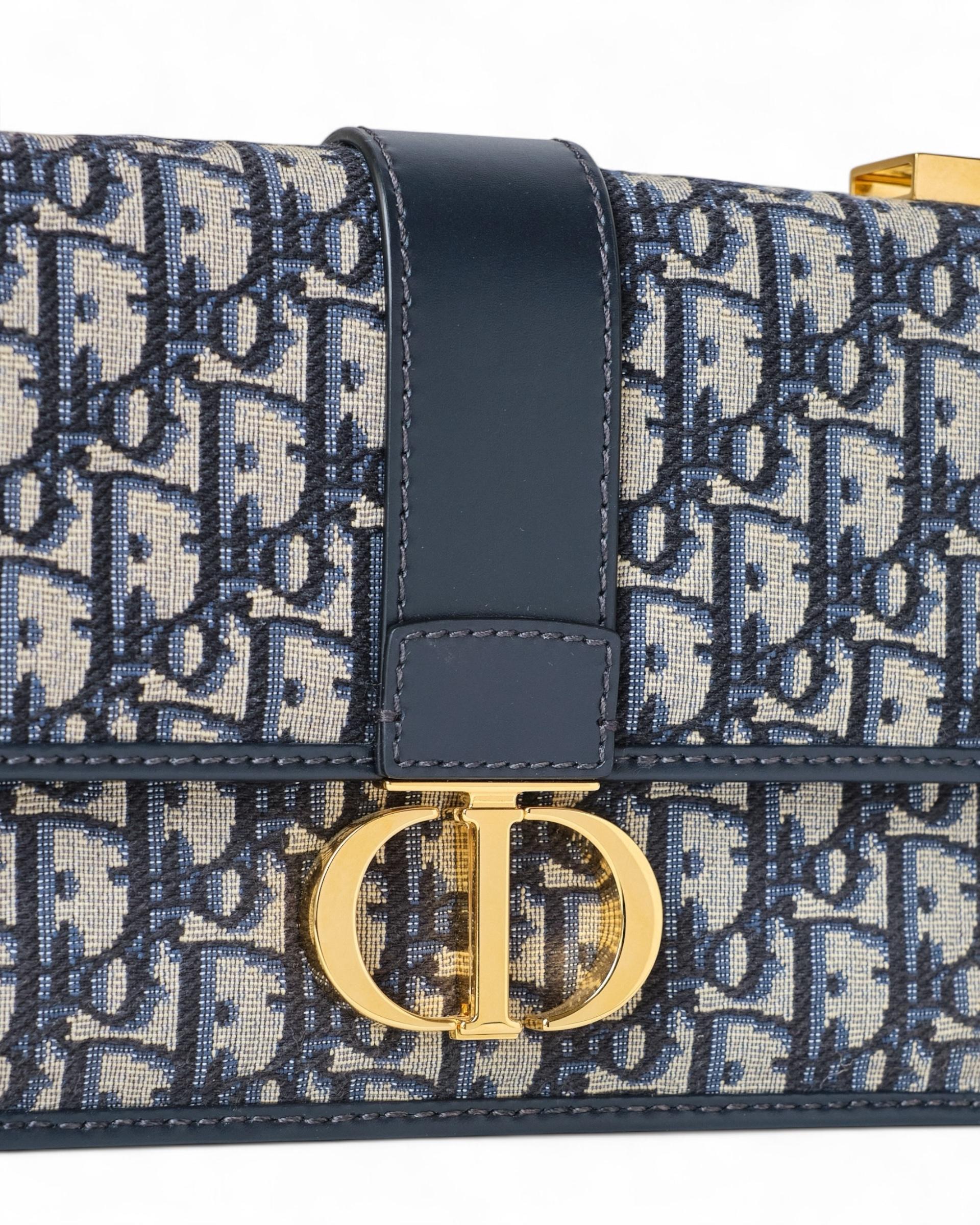 Borsa firmata Dior, modello 30 Montaigne, realizzata in pregiato tessuto Jacquard con inserti in pelle, nella classica fantasia Oblique Blu e con hardware dorato. Il modello presenta una patta frontale decorata con il logo “CD” in metallo e una