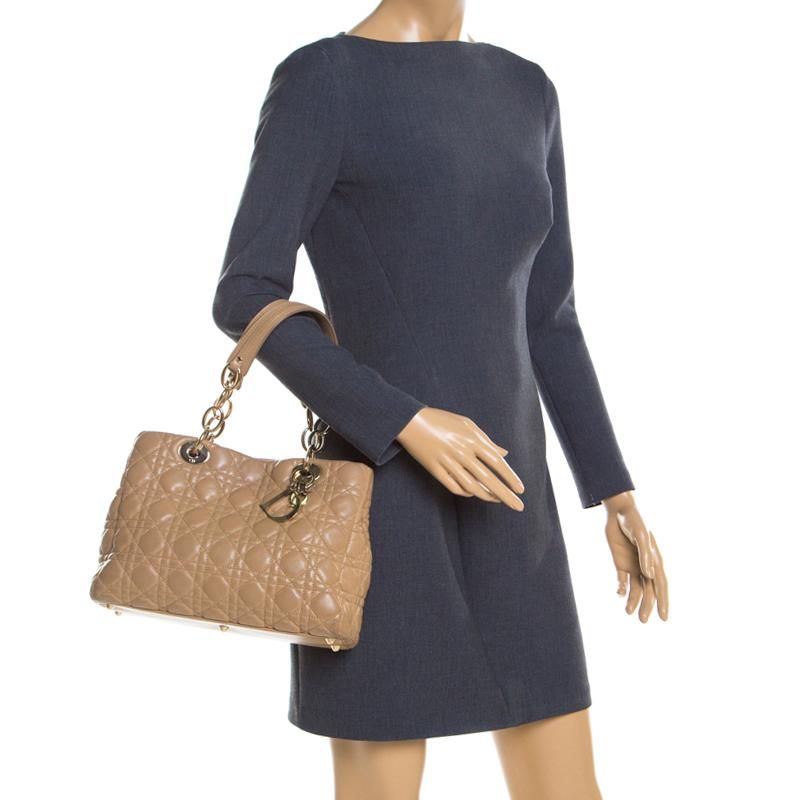 This stylish accessory is exceptionally designed by the fashion house of Christian Dior. Crafted from beige leather, this beauty represents the signature cannage quilt. Adorned with brand lettering at the front, it comes with two top handles and