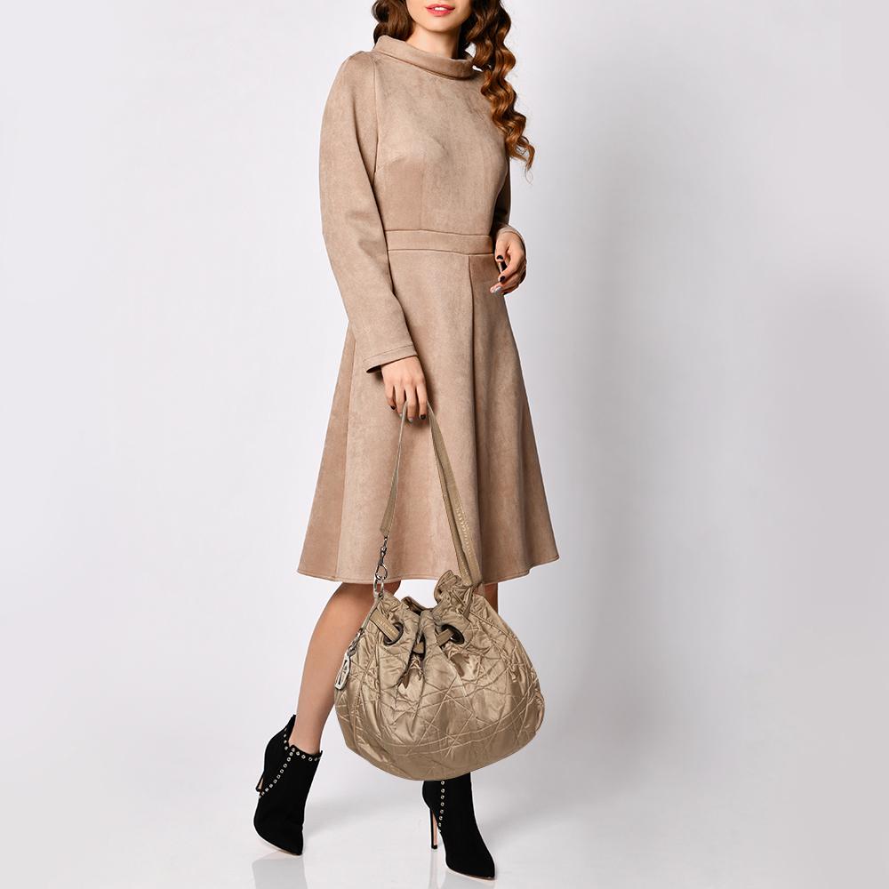 This stylish bag from Dior has been crafted from beige nylon and leather and styled with their signature cannage pattern. The bag features a shoulder strap, a D cutout charm, and a drawstring closure. The insides are fabric lined and spacious enough