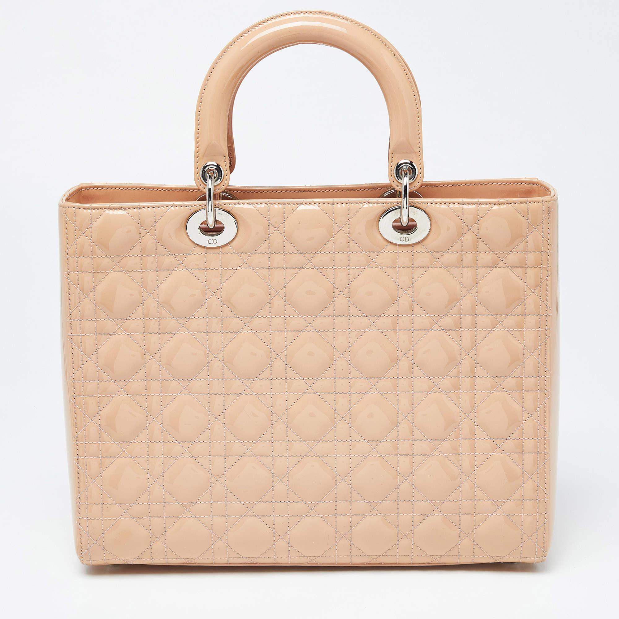 Un statut intemporel et un grand design caractérisent le fourre-tout Lady Dior. Il s'agit d'un sac emblématique dans lequel les gens continuent d'investir à ce jour. Cette beauté classique est réalisée en cuir verni Cannage beige. Le sac est doté