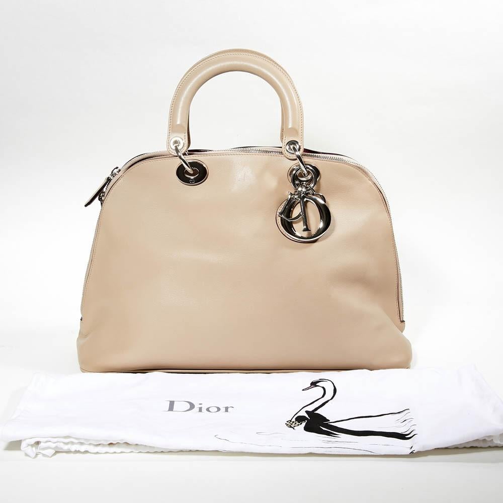 This Dior leather bag comes in a light beige shade with silver-tone hardware (engraved CD) and Dior letter charms. Corners are slightly marked (see pictures). A big compartment that close with a zipper (Two inner compartments) and a  two