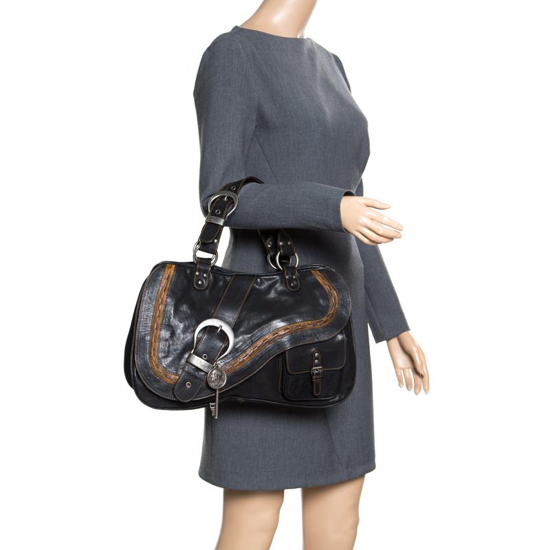 Inspired by the shape of a saddle, the popular rustic style Dior Gaucho shoulder bag is a unique bag to own. The Gaucho bag’s exterior is made from black leather that folds over to resemble an old western saddle. It is accented with an adjustable