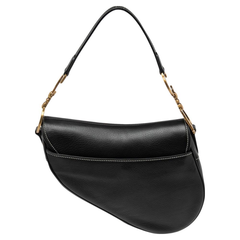 The Saddle bag is one of Dior’s most iconic and popular handbags. This version is made from smooth black leather, that is accented with large Dior gold-tone charms on the shoulder strap and front. Its petite yet spacious interior is lined with nylon