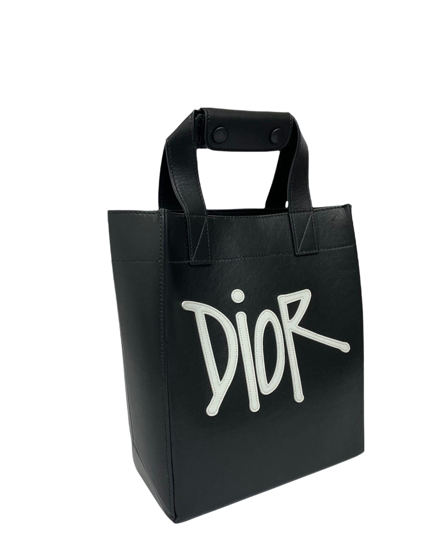 Dior x Shawn Limited Edition tote bag in black and white leather with black hardware.It has a central opening with button closure. The interior is lined with smooth black leather, and also features an internal side pocket.In addition, it is equipped