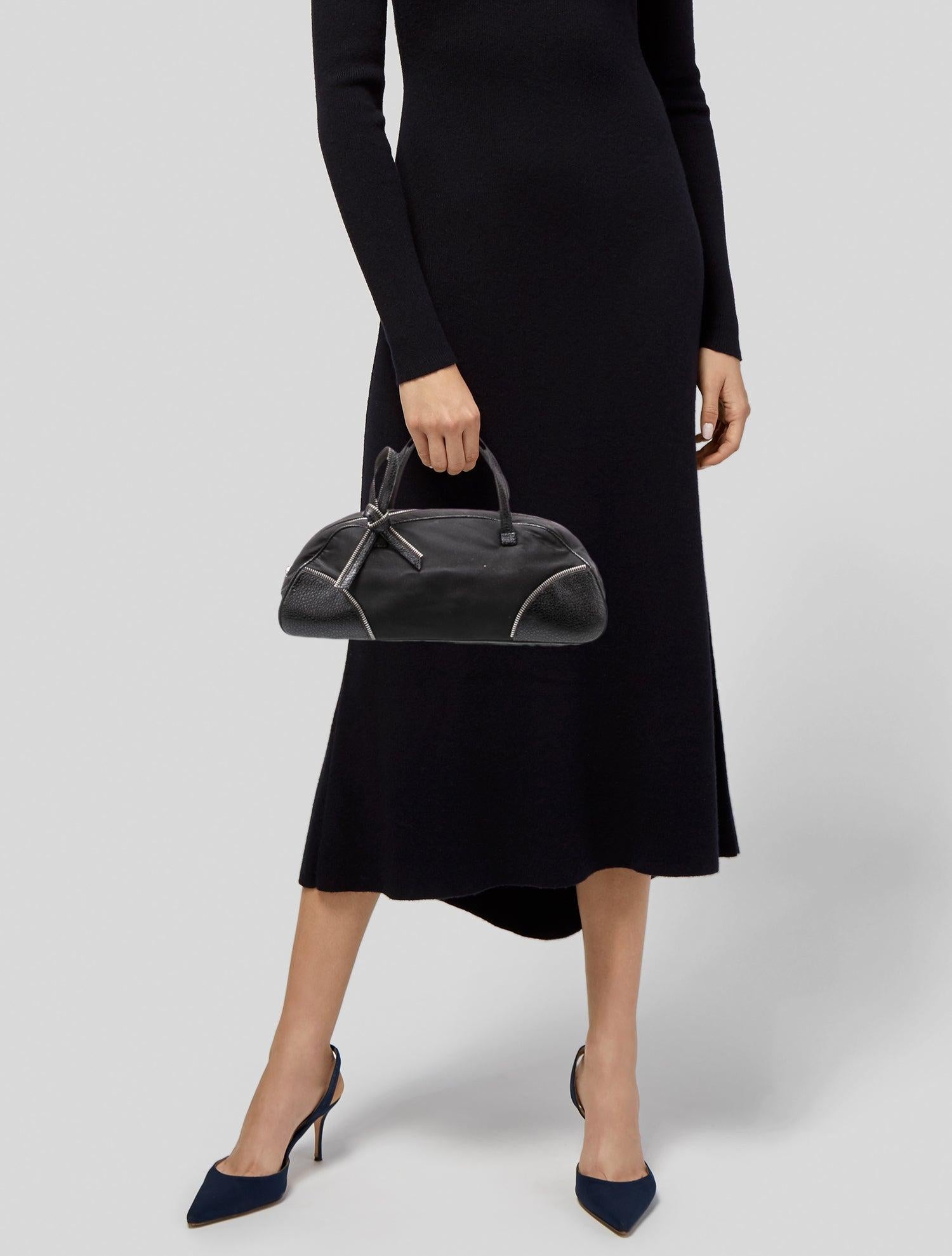 This bag is designed by John Galliano in 2001 and is made of black nylon with leather finishes. Details include Galliano’s signature zipper embroidery throughout the bag. It features a zip bow embellishment at the top, silver-tone hardware,